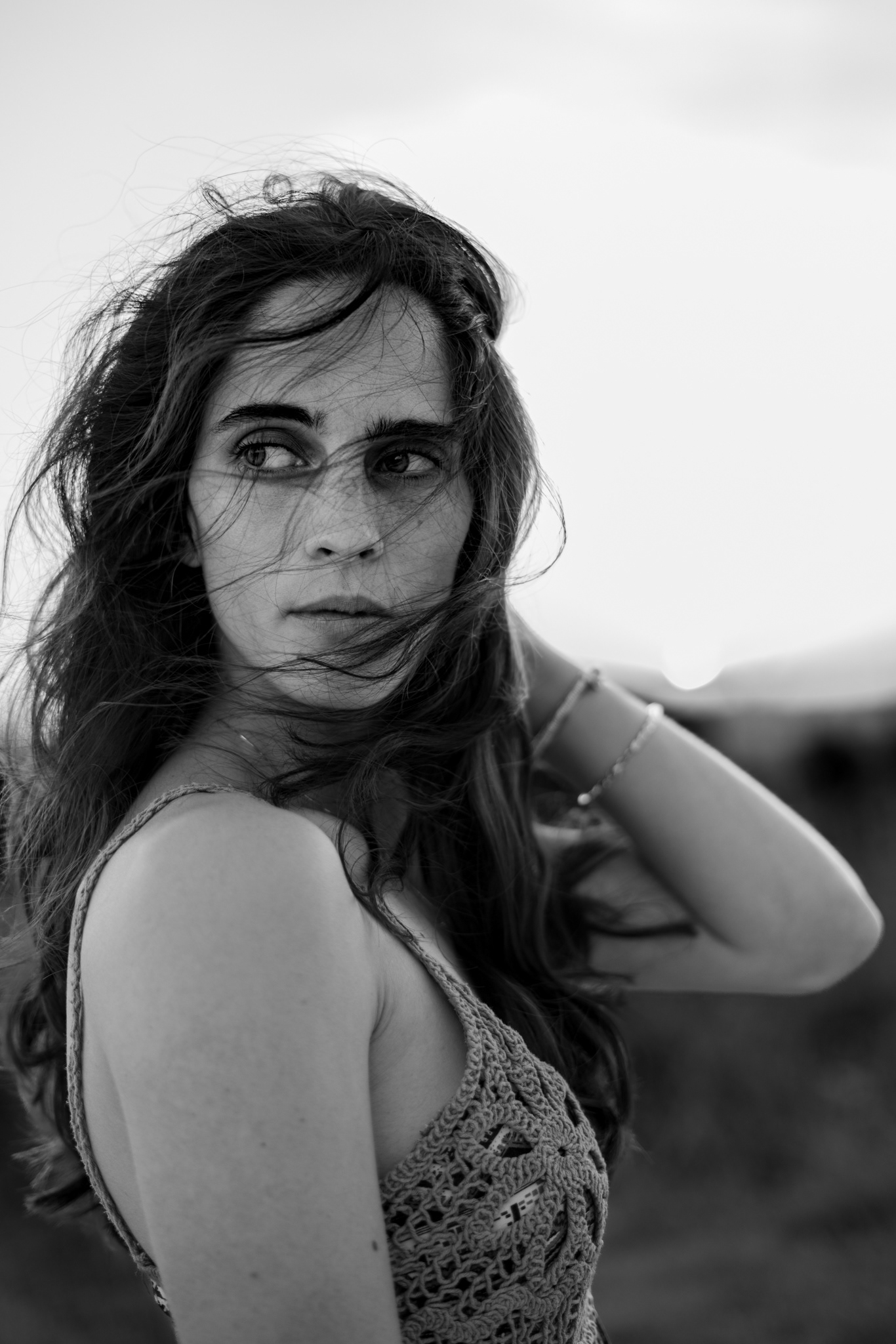Black and white portrait of a woman with windblown hair, gazing to the side, conveying emotion and natural beauty in an outdoor setting.