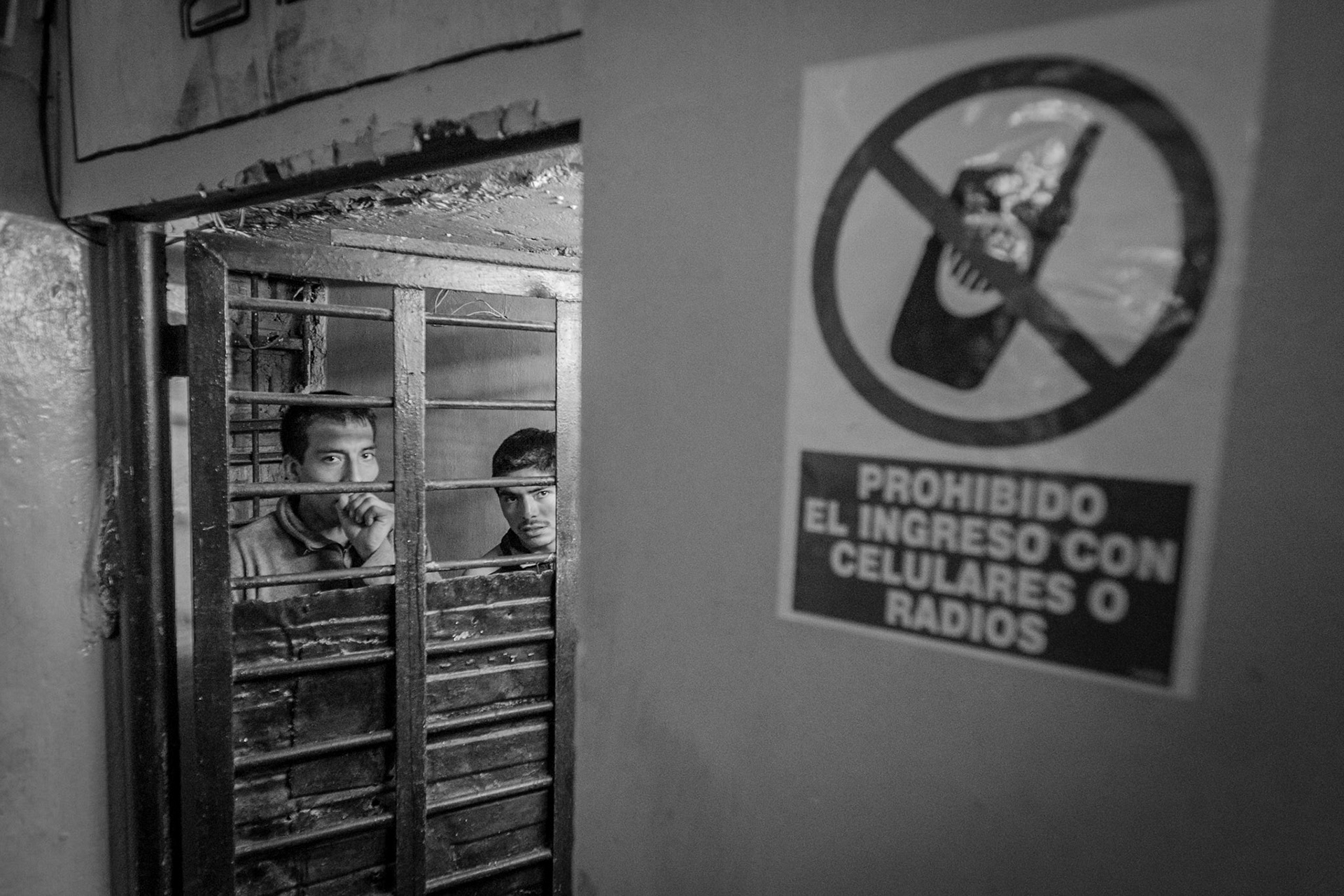 LURIGANCHO PRISON, SAN JUAN DE LURIGANCHO, LIMA, PERU: Contradictory sign prohibiting cell phones at the entrance to one of the cells. Behind the bars, two prisoners on security duty.