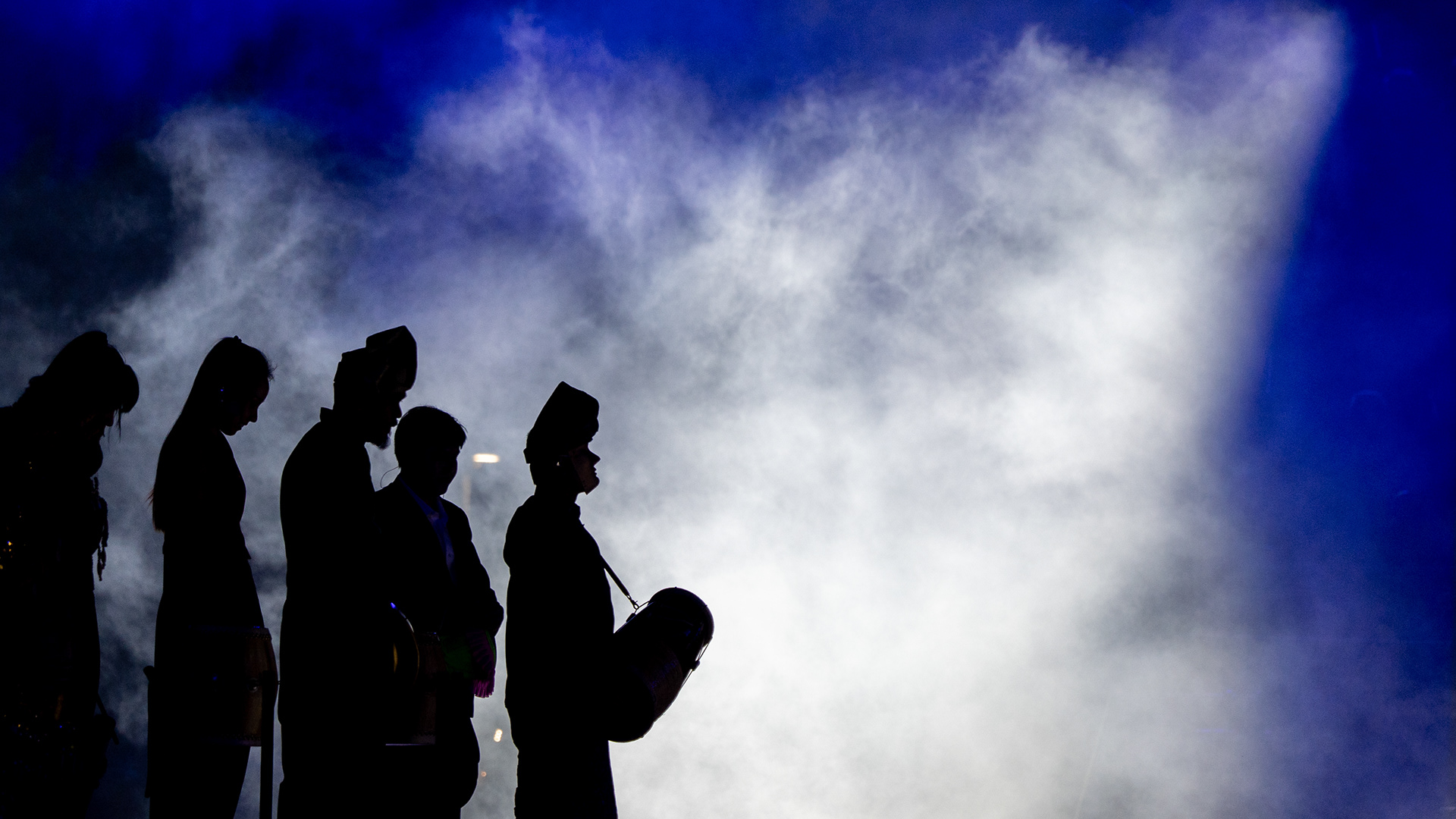 Stillness Out of Smoke.  Performers wait in silhouette as stage smoke fills the beam. Chingay Parade, Singapore, 2026