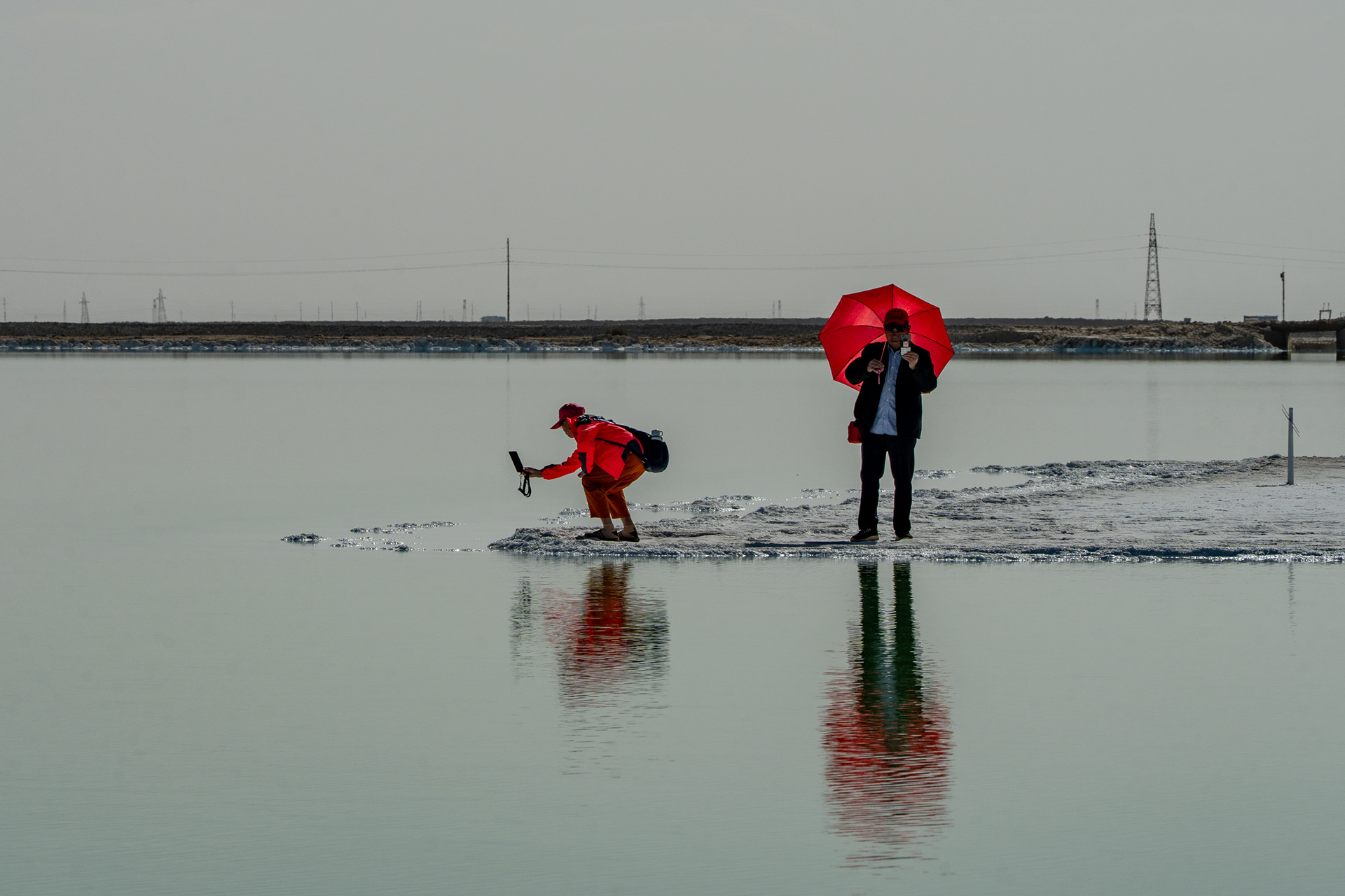  The Red Umbrella. Two visitors photograph the salt flat; a single red note on a silver field. Qinghai. China, 2026.