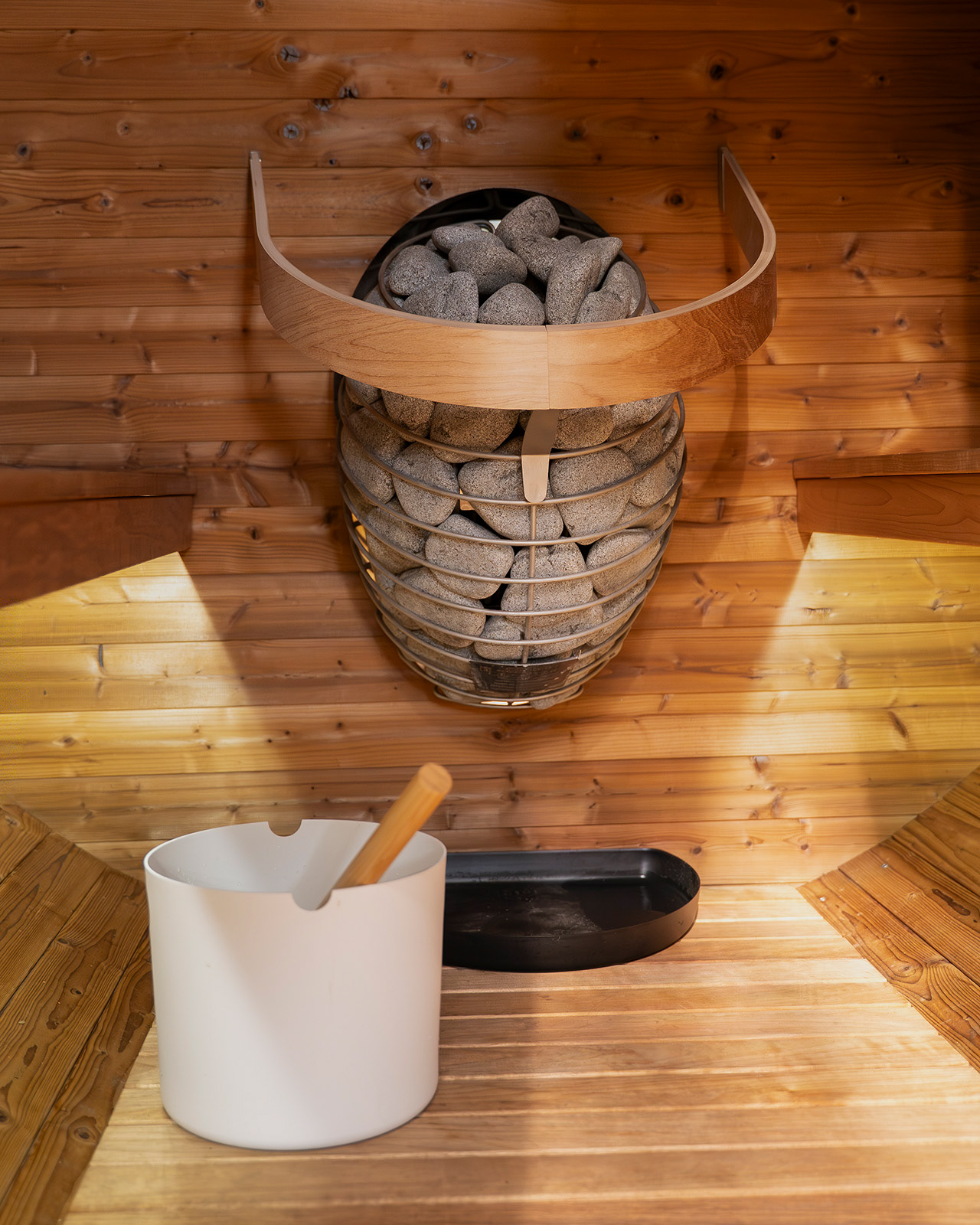 A close-up detail inside the sauna at Roost Merthyr Tydfil, showing the sauna stones and white bucket against the light wood panelling. A warm, natural space for relaxing during a South Wales glamping stay.