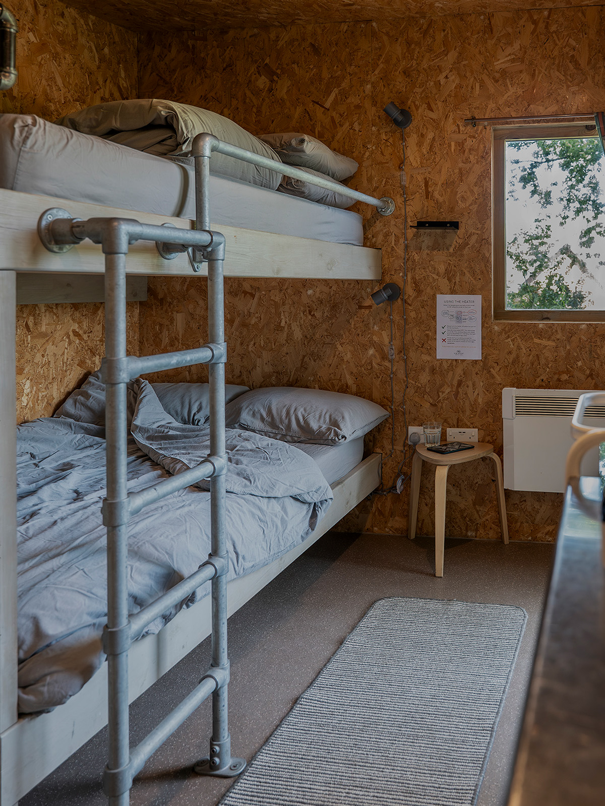 A relaxed bedroom detail inside Arosfa cabin at Roost Merthyr Tydfil, showing the bunk bed with a slightly rumpled duvet, as though a guest has just got up. A glimpse of the informal, homely feel of this South Wales glamping accommodation.