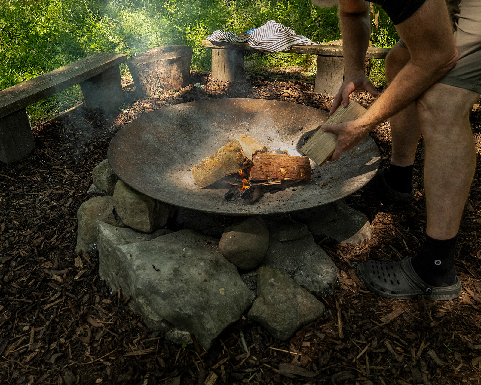 A host tending the fire pit at Roost Merthyr Tydfil, adding logs to the fire and creating a warm outdoor setting for guests staying in the South Wales glamping cabins.