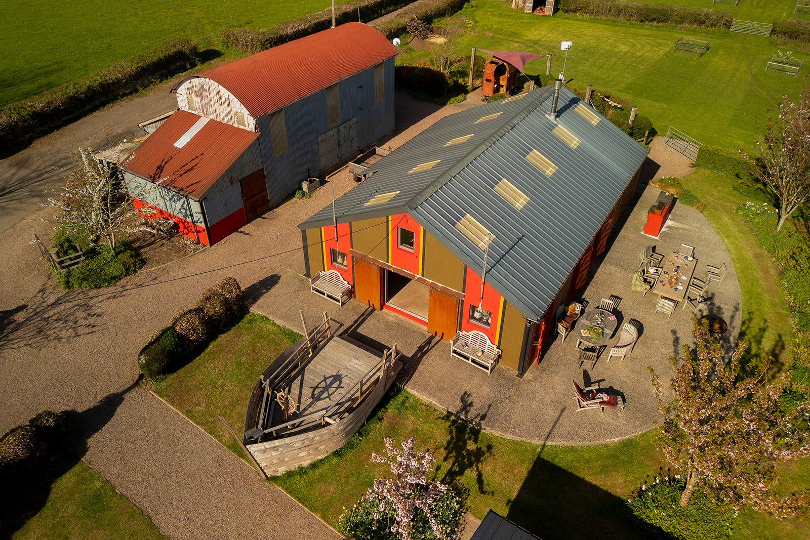 Aerial hospitality photography of The Pavilion at Woodlands Farm Wales, showing the outdoor dining and seating area alongside the replica pirate ship.
