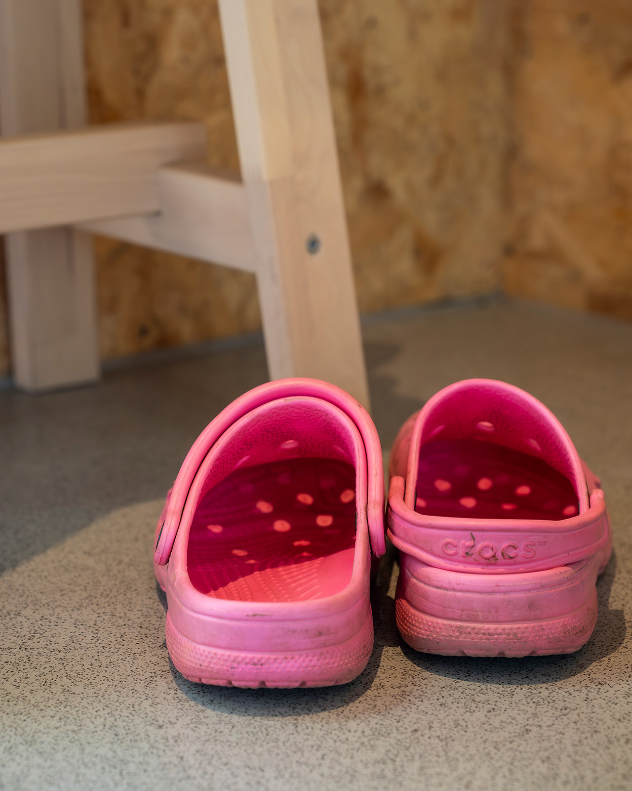 A close-up of pink Crocs beside a wooden stool in one of the bathrooms at Roost Merthyr Tydfil, capturing a small, practical detail of this South Wales glamping accommodation.
