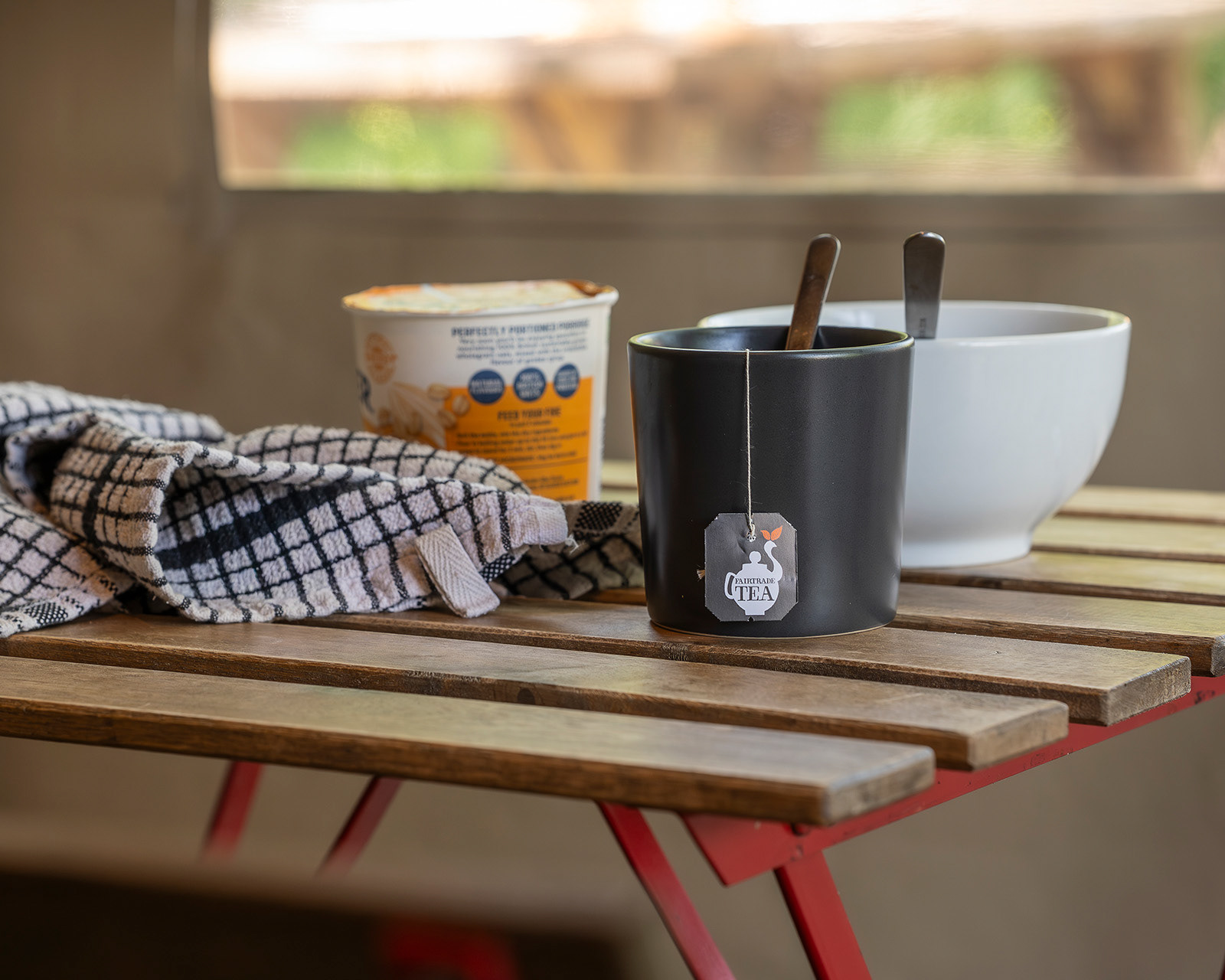 A cosy breakfast detail in the kitchen at Roost Merthyr Tydfil, with a black mug, teabag and spoon, a plastic container of instant porridge and a kitchen towel on the small table. A simple start to the day at this South Wales glamping accommodation.