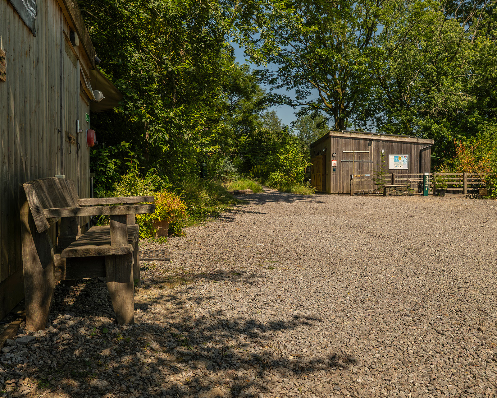 The gravel parking area at Roost Merthyr Tydfil, with the guest shower block visible in the distance and surrounded by trees and greenery. A peaceful arrival area for guests staying at this South Wales glamping accommodation.