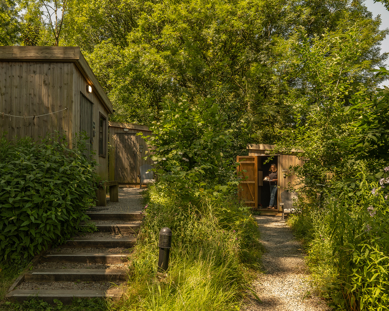 A wider view of the glamping cabins at Roost Merthyr Tydfil, with a host stepping out from one of the cabins. The relaxed setting highlights the thoughtfully designed outdoor spaces at this South Wales glamping accommodation.