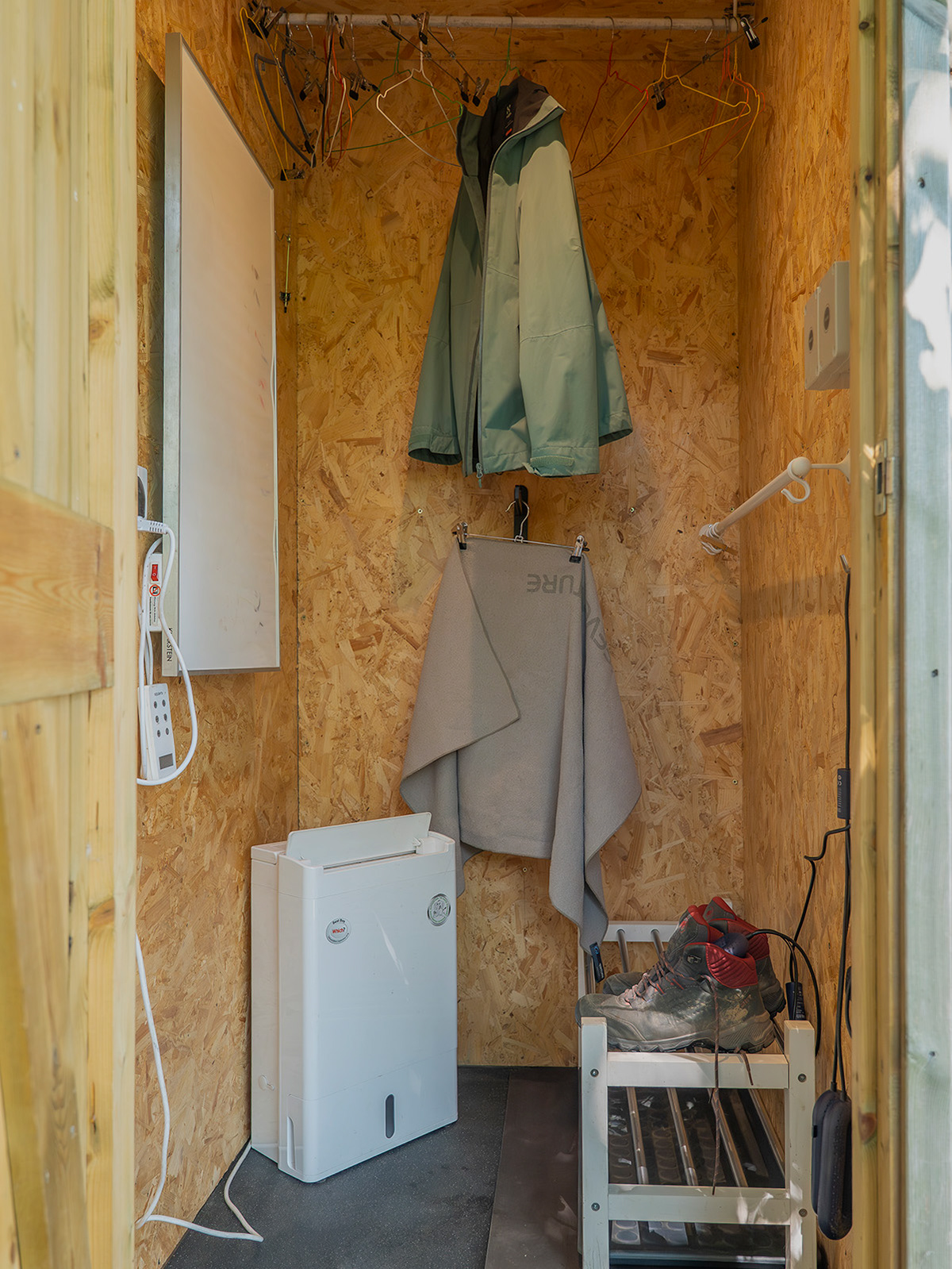 The full drying room at Roost Merthyr Tydfil, with jackets and hangers, walking boots on the boot rack and towels ready to dry. A heater and wall-mounted drying panel help keep wet outdoor clothing and footwear warm and dry after exploring the South Wales countryside.