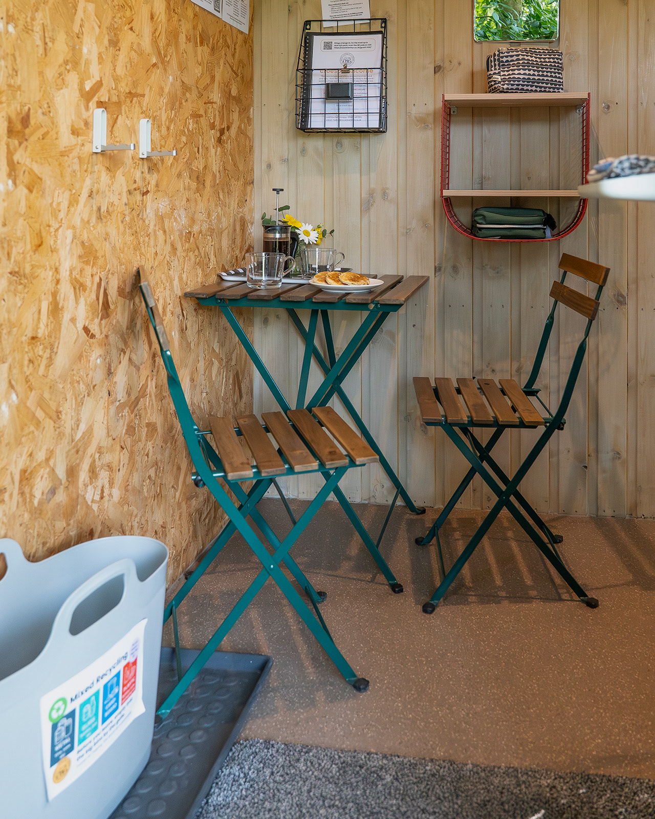 The dining area inside Arosfa cabin at Roost Merthyr Tydfil, with a small table set for two, fresh coffee in a cafetiere and traditional Welsh cakes. A cosy space for enjoying breakfast or a relaxed coffee during a South Wales glamping stay.