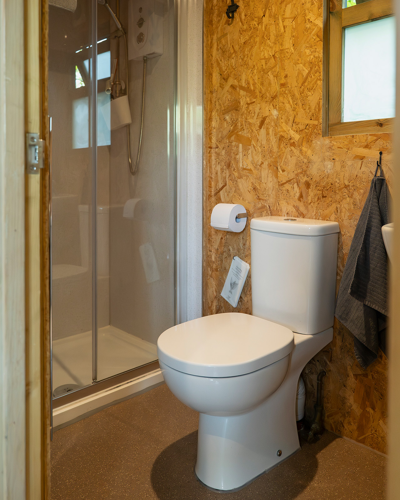 The en-suite bathroom in Arosfa cabin at Roost Merthyr Tydfil, showing the shower, toilet and fresh towel, with natural light coming through the window. A practical and comfortable bathroom for guests staying at this South Wales glamping accommodation.