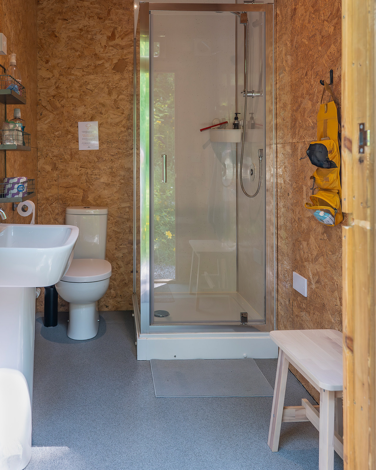 The interior of the bathroom at Roost Merthyr Tydfil, with a shower, toilet, washbasin and small stool, alongside a yellow hanging travel toiletry bag. A practical and well-equipped space for guests staying at this South Wales glamping accommodation.