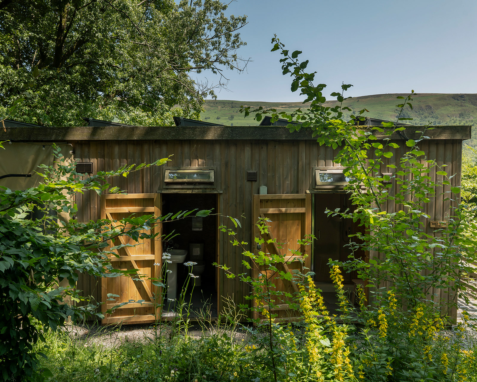 The exterior of Bathrooms 1 and 2 at Roost Merthyr Tydfil, set among the surrounding greenery with views towards the hills beyond. A peaceful setting for guests staying at this South Wales glamping accommodation.