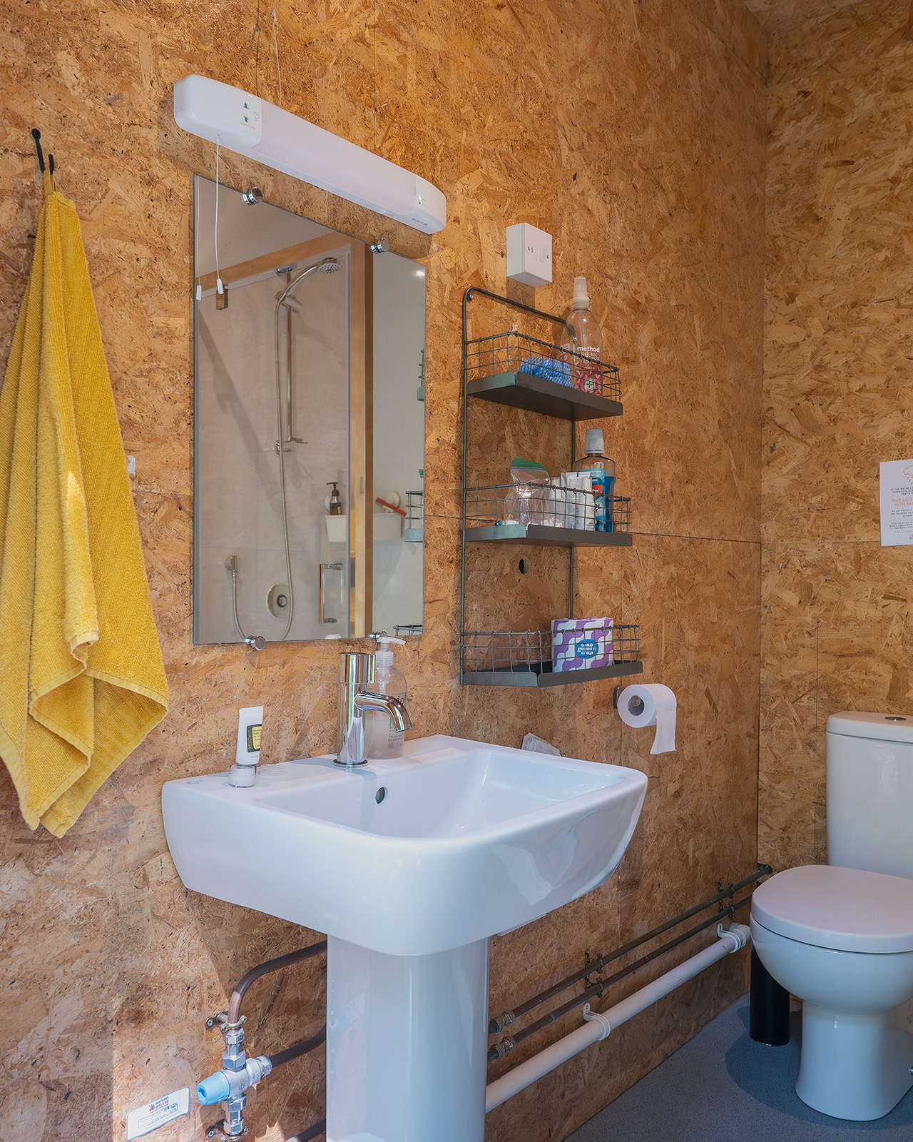 A bright bathroom detail at Roost Merthyr Tydfil, showing the washbasin, mirrors, yellow towel and toiletries arranged on the shelves. A simple and practical space for guests staying at this South Wales glamping accommodation.