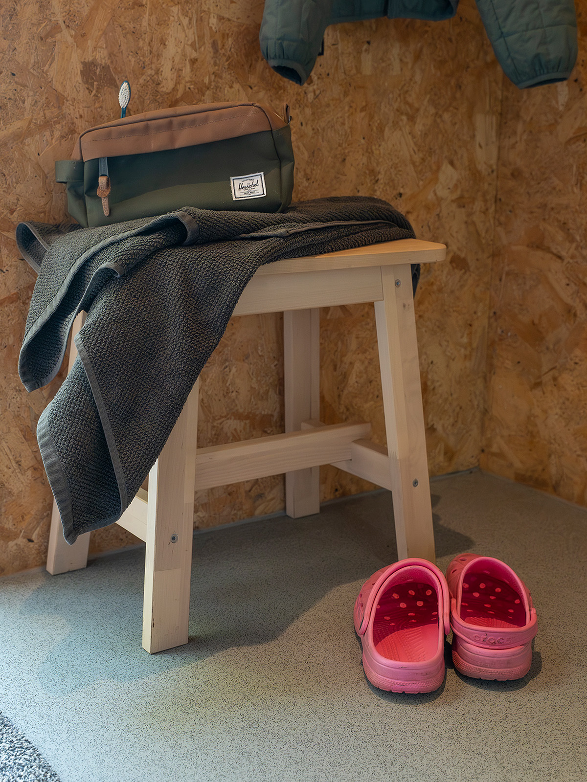 A cosy bathroom detail at Roost Merthyr Tydfil, with a dark grey towel and toiletry bag on a wooden stool and a pair of pink Crocs beside it. Practical touches for a comfortable stay at this South Wales glamping accommodation.