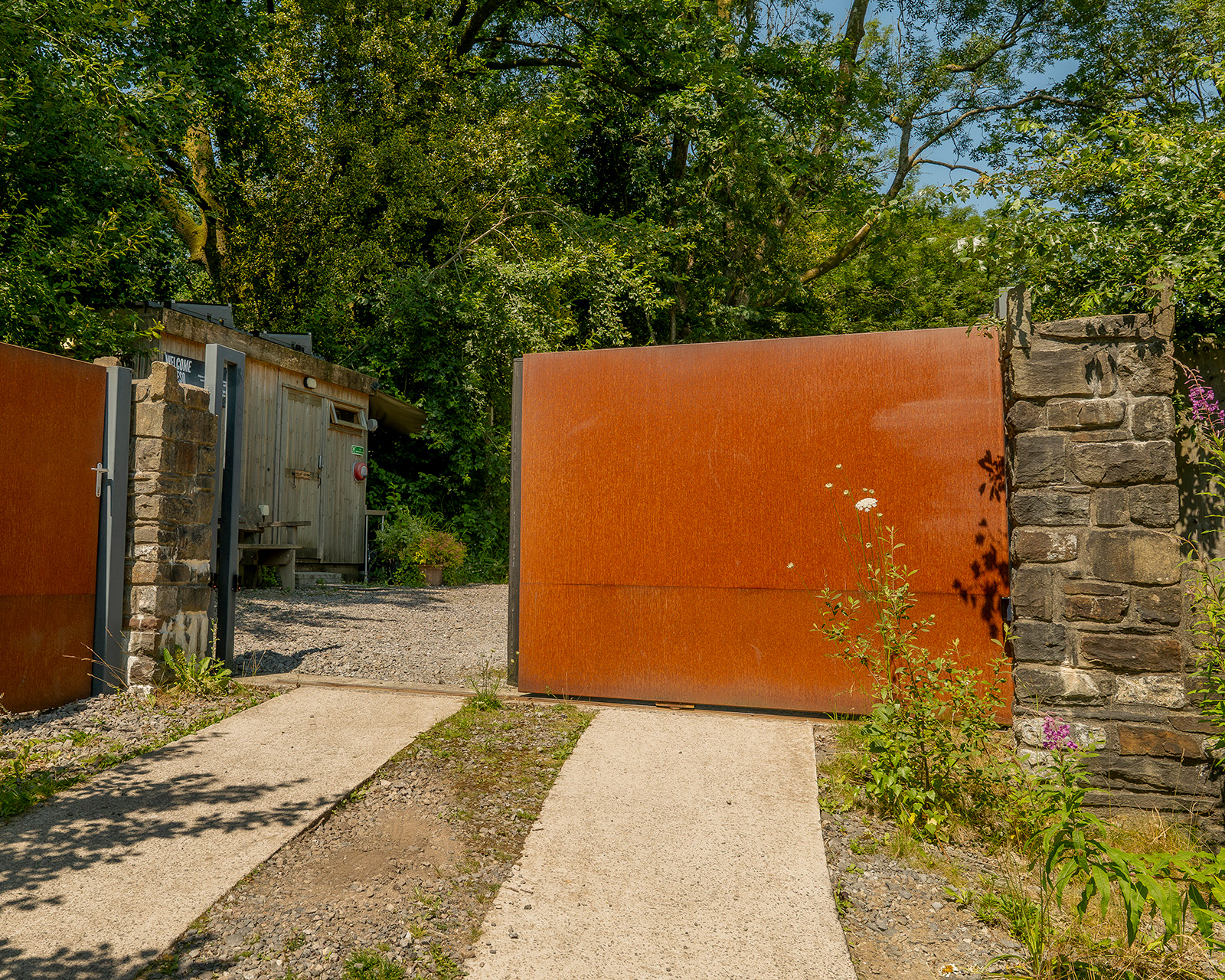 The entrance to Roost Merthyr Tydfil, with the gate partially open and a glimpse of the guest parking area beyond. A welcoming arrival point for this South Wales glamping accommodation.