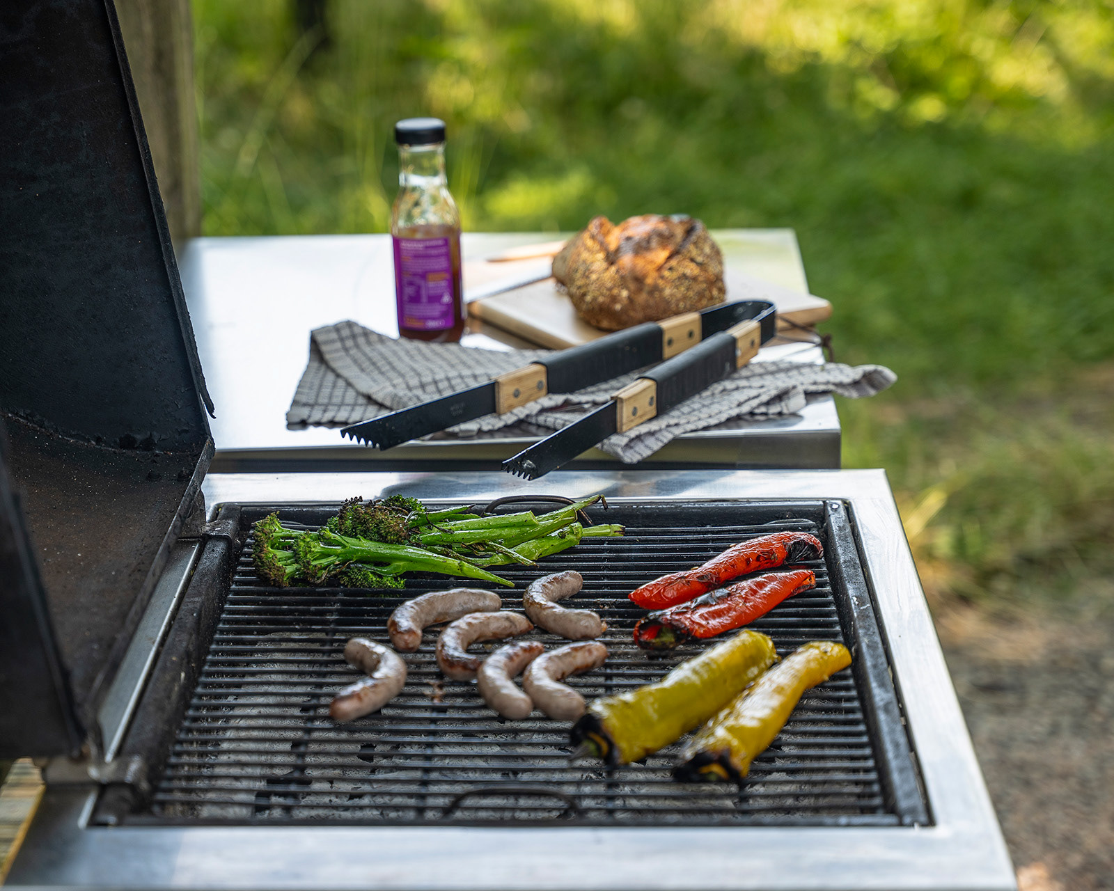 Food cooking on the outdoor BBQ at Roost Merthyr Tydfil, with sausages, red and yellow peppers, bread and sauce ready for a relaxed al fresco meal at this South Wales glamping accommodation.
