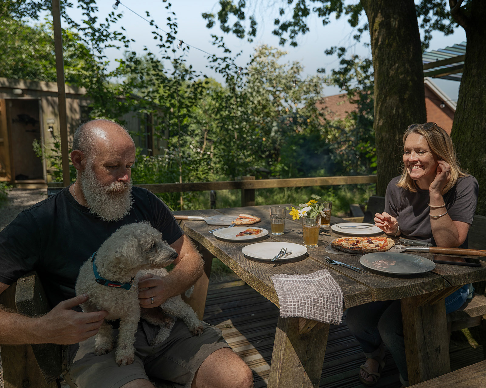 Hosts enjoying pizza and drinks at the outdoor picnic table at Roost Merthyr Tydfil, with their dog joining them. A relaxed, dog-friendly glamping stay in South Wales.