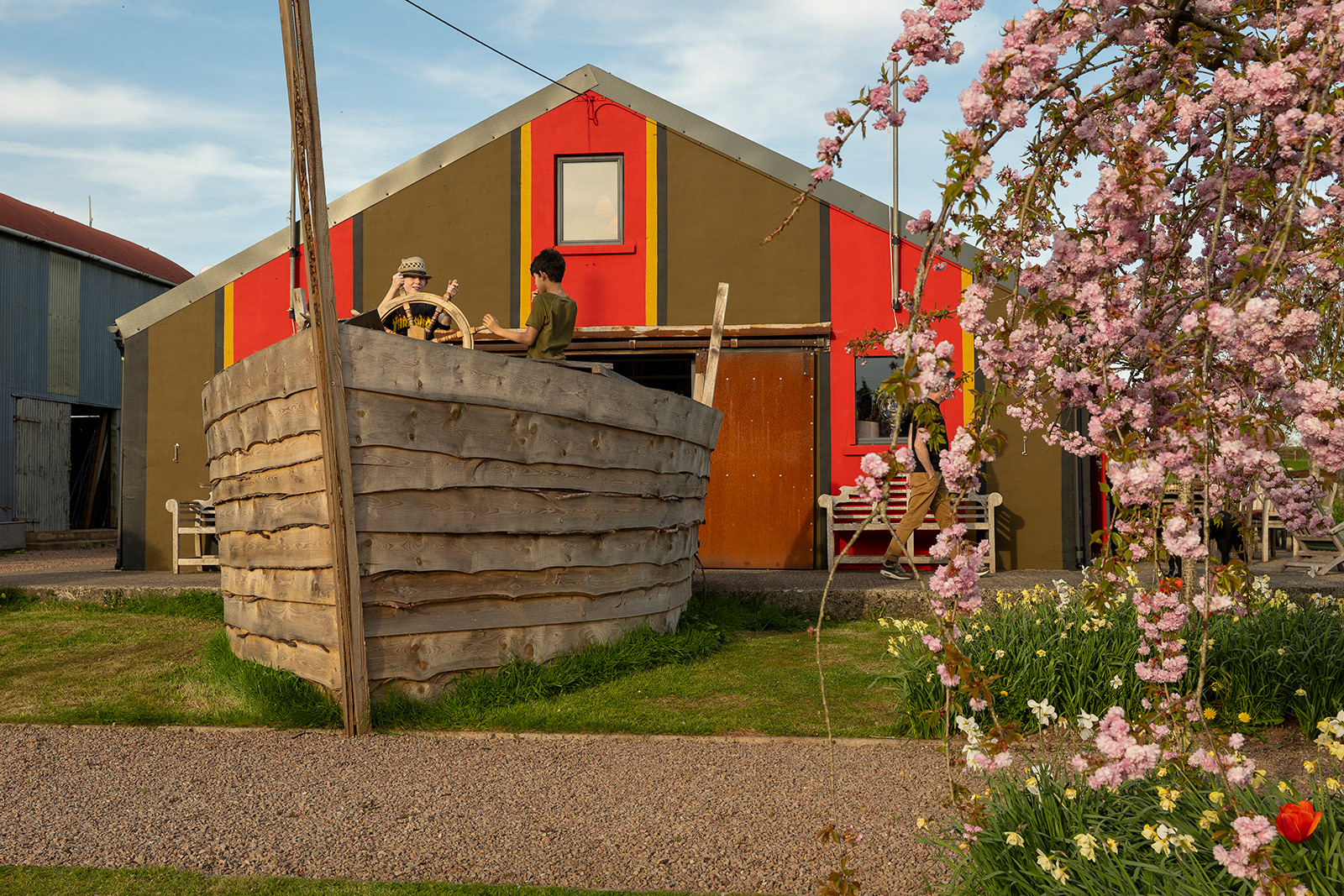 Outdoor activities at Woodlands Farm Wales, with young guests exploring the replica ship beside The Pavilion, framed by a flowering ornamental cherry tree.