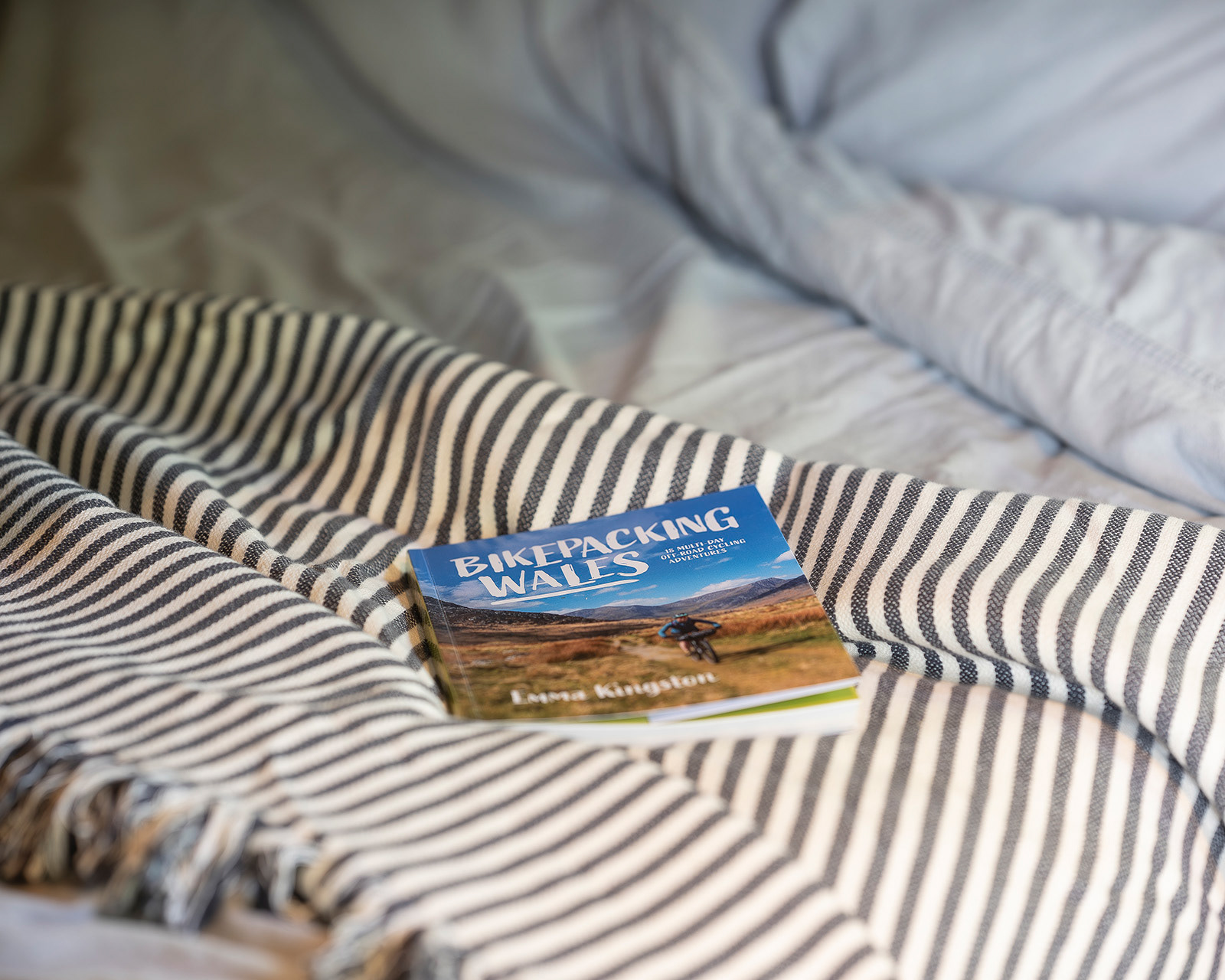 A copy of Bikepacking in Wales resting on a blanket at Roost Merthyr Tydfil, photographed with a shallow depth of field to capture the relaxed atmosphere of this South Wales glamping accommodation.