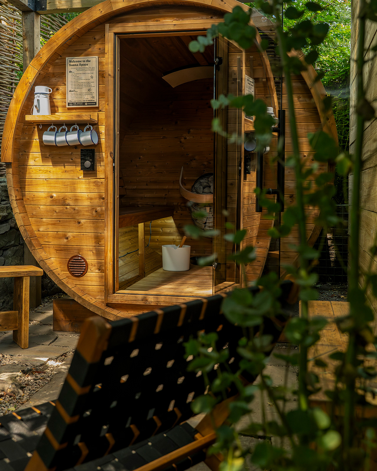The round sauna building at Roost Merthyr Tydfil, with a wooden garden chair outside and surrounded by natural greenery. A peaceful space to relax and unwind during a South Wales glamping stay.