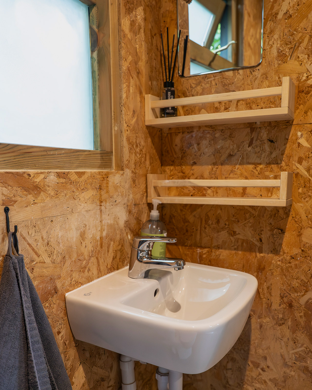 A detail of the en-suite bathroom in Arosfa cabin at Roost Merthyr Tydfil, showing the washbasin, mirror, shelving and fresh towel beside the window. A practical and welcoming space within this South Wales glamping accommodation.
