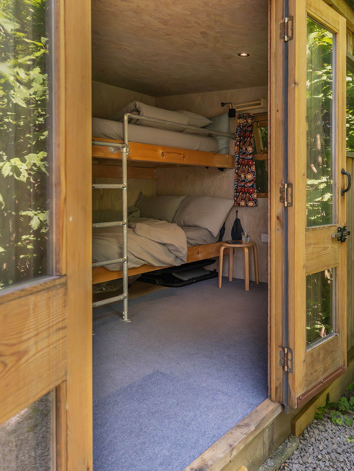 The bunk beds inside Gwynfa cabin at Roost Merthyr Tydfil, photographed from outside through the open doorway. The inviting view into the cosy sleeping space offers a glimpse of the relaxed, welcoming atmosphere of this South Wales glamping accommodation.