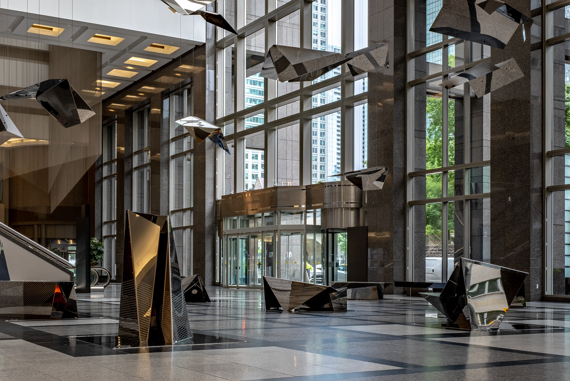 Vue au niveau du sol du hall d'entrée du 1000 de la Gauchetière conçu par Lemay et Dimakopoulos & Associates. Le riche calepinage au sol en pierre accompagne les colonnes massives, l'installation d'Atelier in situ et les grandes portes tournantes vitrées.