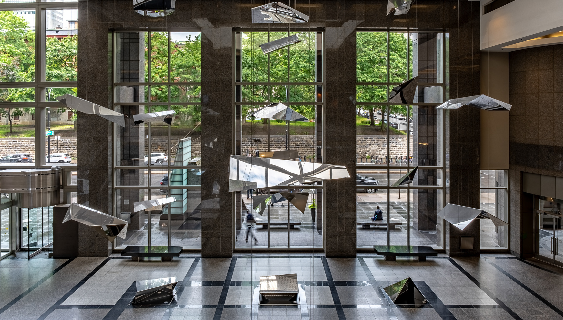 Vue en plongée illustrant la grandeur architecturale du hall d'entrée du 1000 de la Gauchetière à Montréal. Le calepinage contrasté au sol en granit est surmonté par les éléments sculpturaux d'Atelier in situ flottant devant la rue.