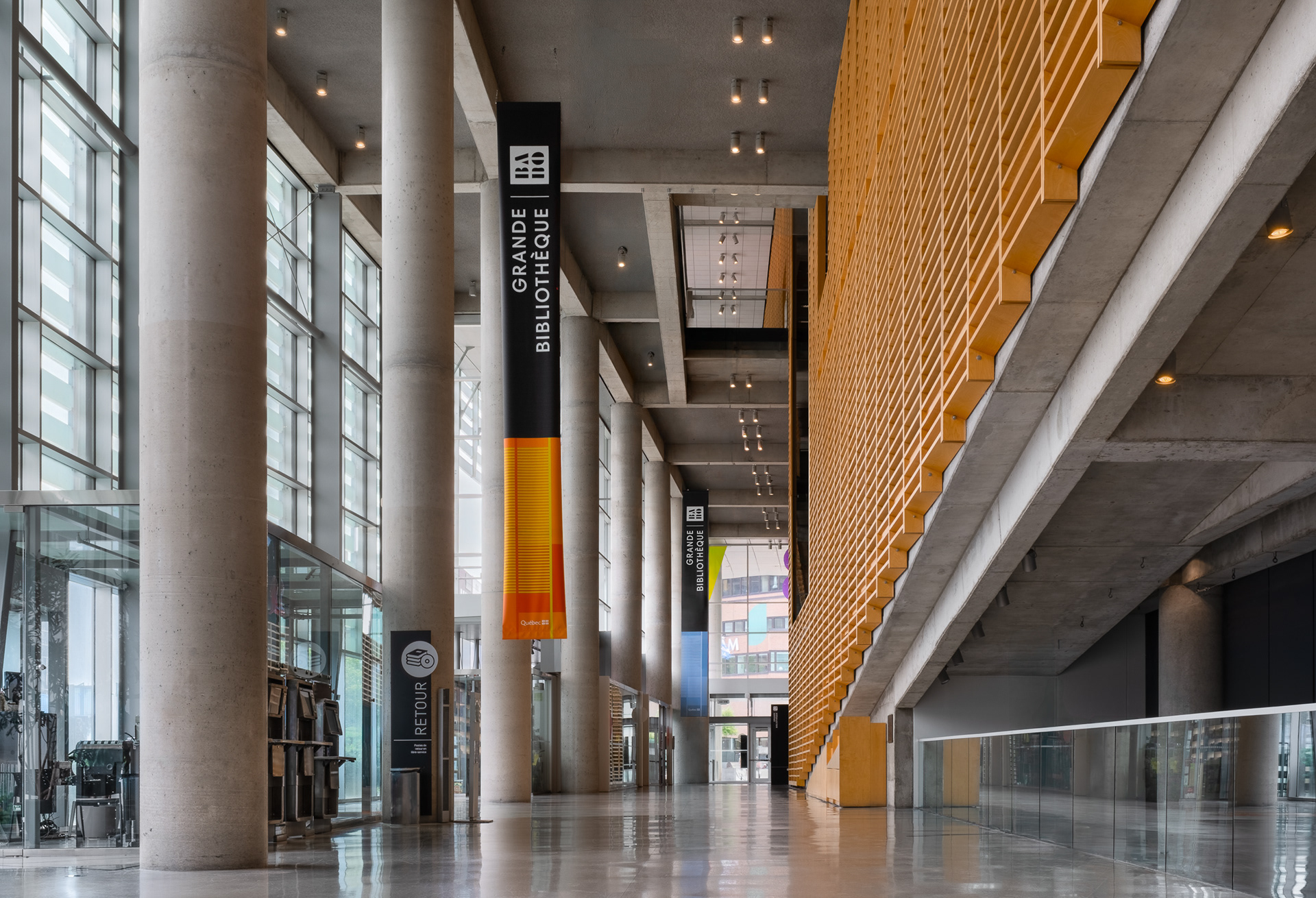 Vue du hall principal de la Grande Bibliothèque à Montréal par Patkau Architects et partenaires. L'espace de circulation met en valeur des colonnes en béton massif, un plafond structurel apparent et de grandes parois à claires-voies en bois.