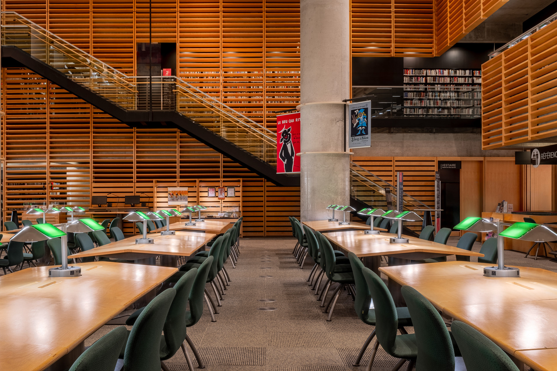 Vue d'ensemble de la chambre de bois de la Collection nationale à la Grande Bibliothèque. L'espace de lecture est entouré d'imposantes parois en claires-voies de bois intégrant un escalier métallique menant aux étages supérieurs.