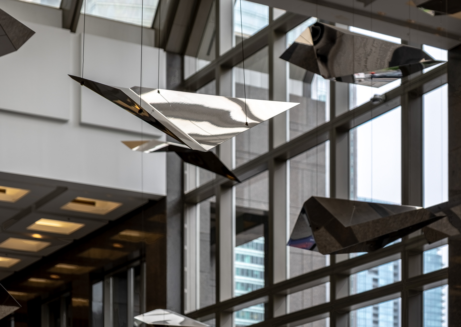 Gros plan sur l'installation d'art public au cœur du hall du 1000 de la Gauchetière à Montréal. Les sculptures asymétriques en métal poli reflètent la lumière naturelle traversant la haute fenestration de l'édifice commercial.