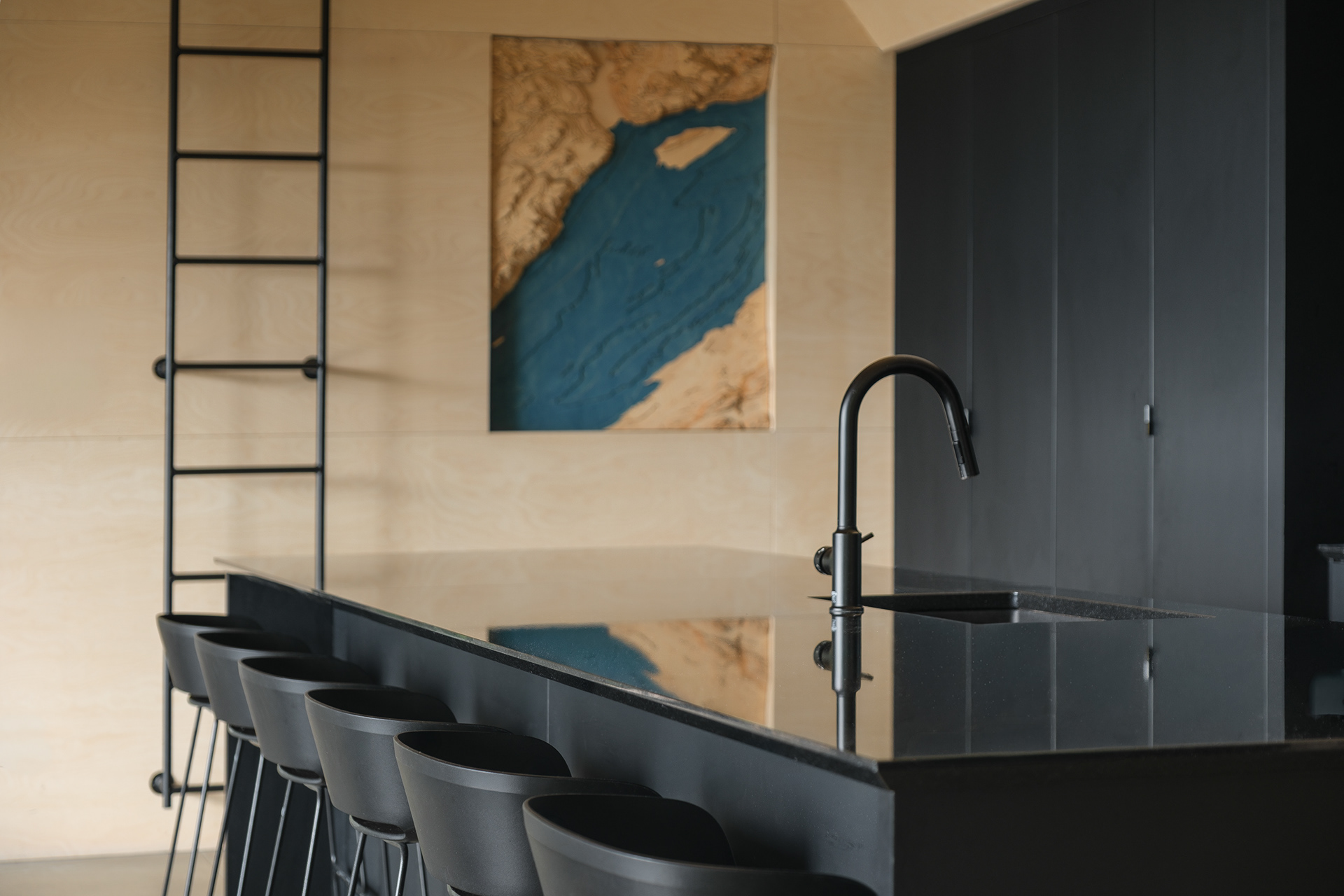 Cuisine contemporaine de la Cabine-A à Charlevoix par Bourgeois / Lechasseur. Un îlot central et des armoires noir mat contrastent élégamment avec les murs en bois clair et une œuvre d'art topographique texturée du fleuve Saint-Laurent.