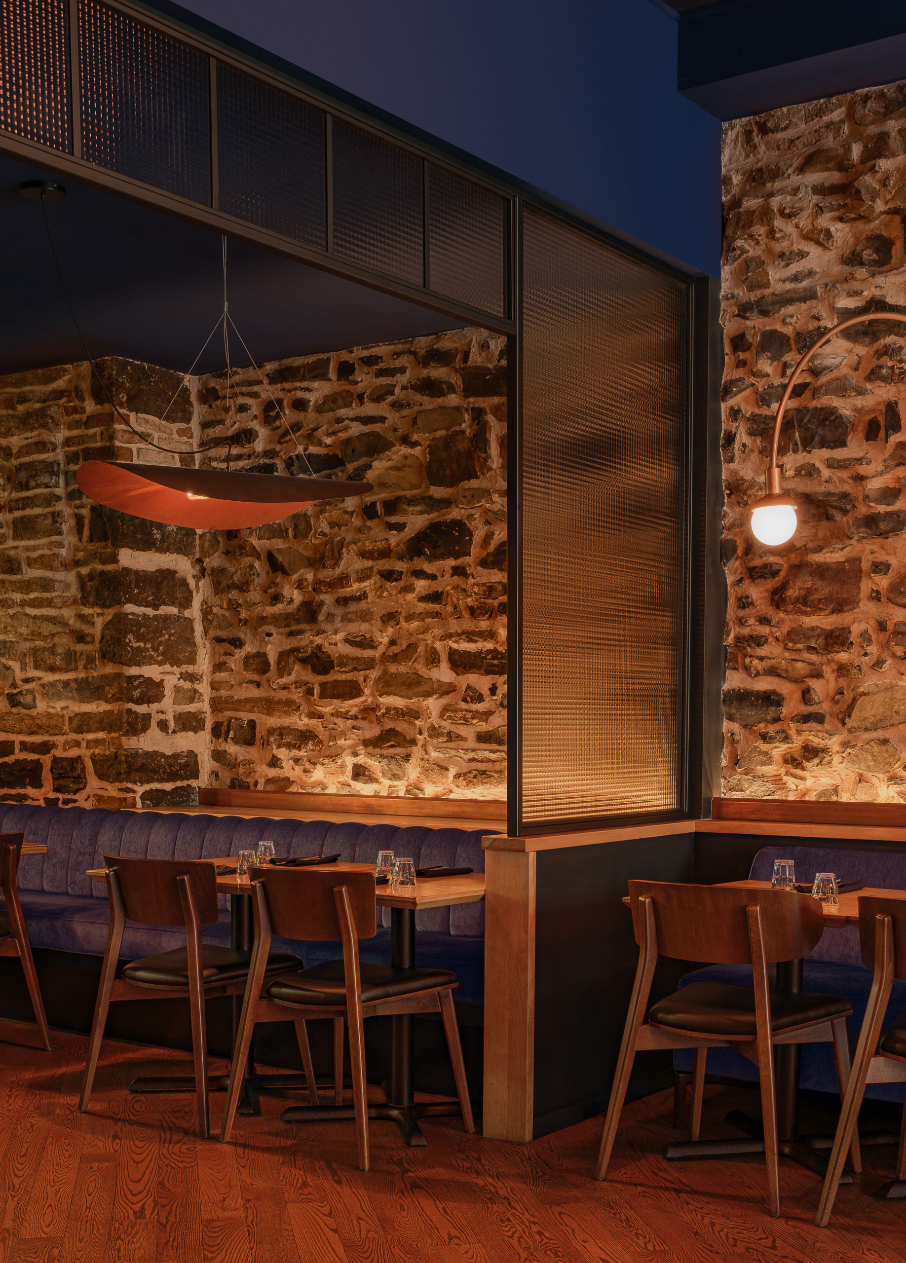 Perspective de l'aménagement du restaurant Kwizinn à Montréal par Taktik Design. Une cloison en verre texturé sépare les banquettes bleues, mises en valeur par un grand luminaire suspendu en cuivre et un mur de pierre brute.