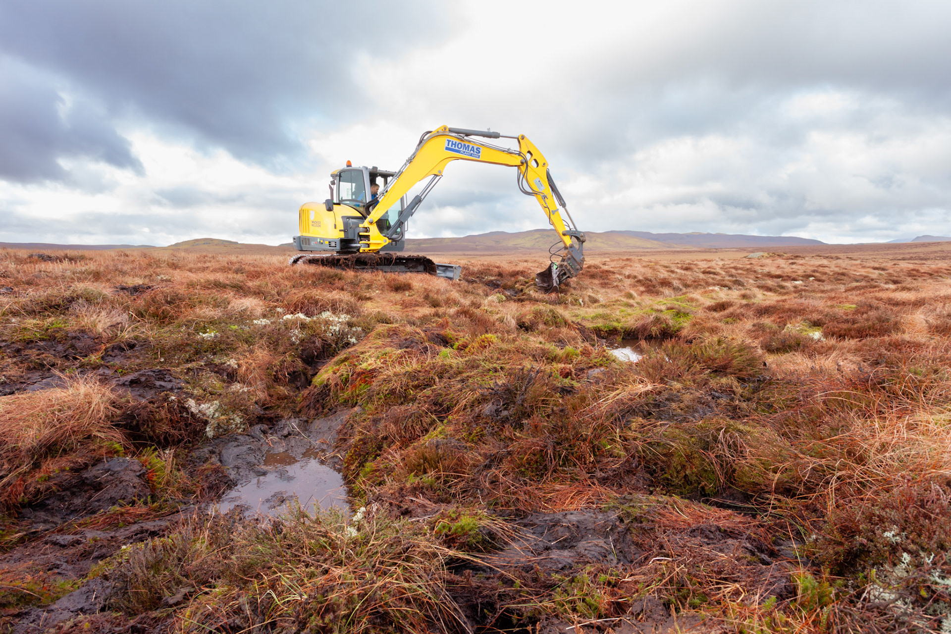 Contractor using digger to carry out peatland restoration work for RSPB peatland restoration project. Winter, Migneint moors, North Wales,UK.