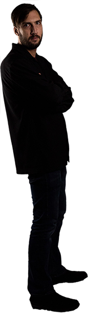 Alex Lindskog photograph standing with arms crossed, facing right, dressed in black, exuding a confident rock star attitude.