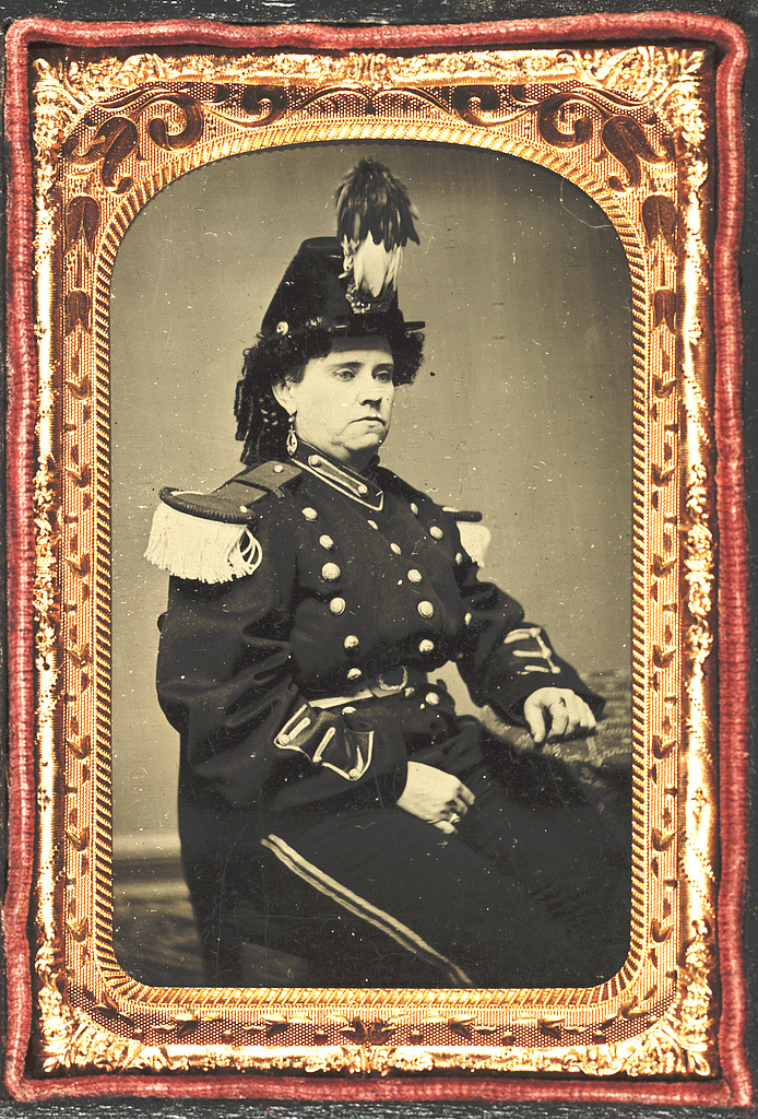 A vintage photo of a person sitting in a military uniform, surrounded by a gold frame.