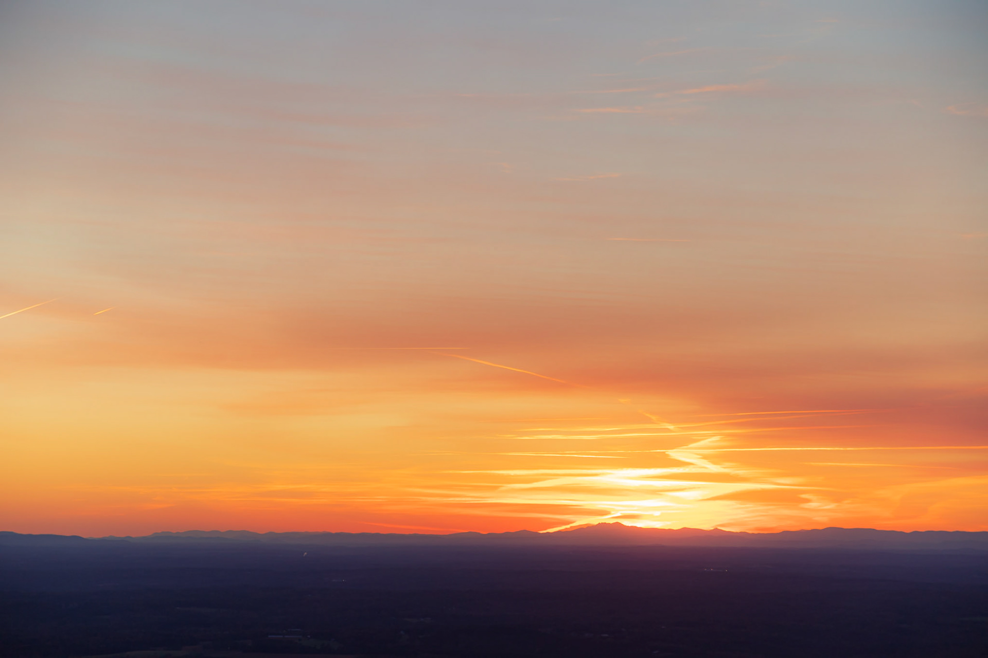 Sunset over the horizon with colorful sky and dark purple mountains.
