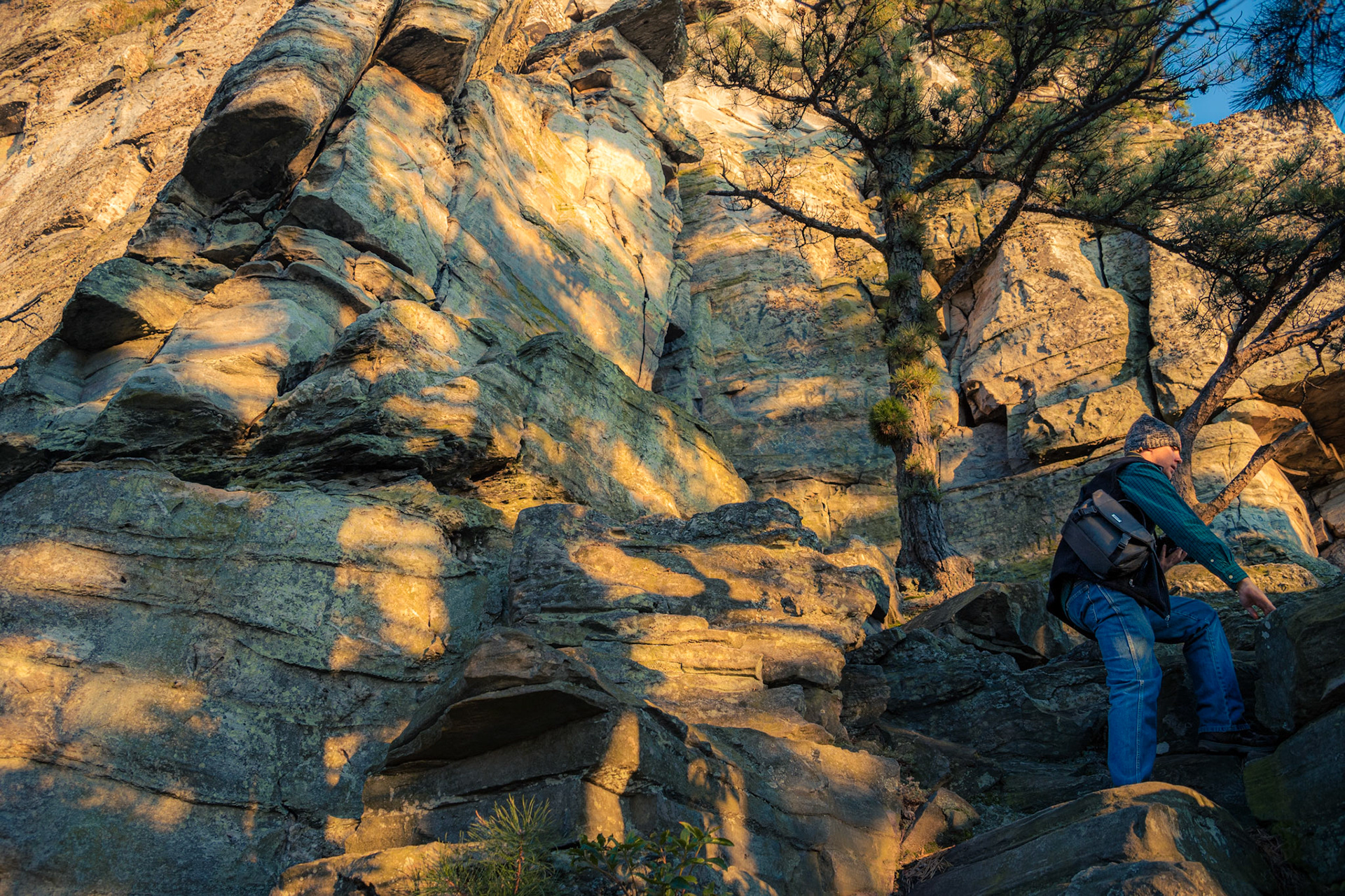 A person climbing rocks with the sunset casting shadows on the large rock behind.