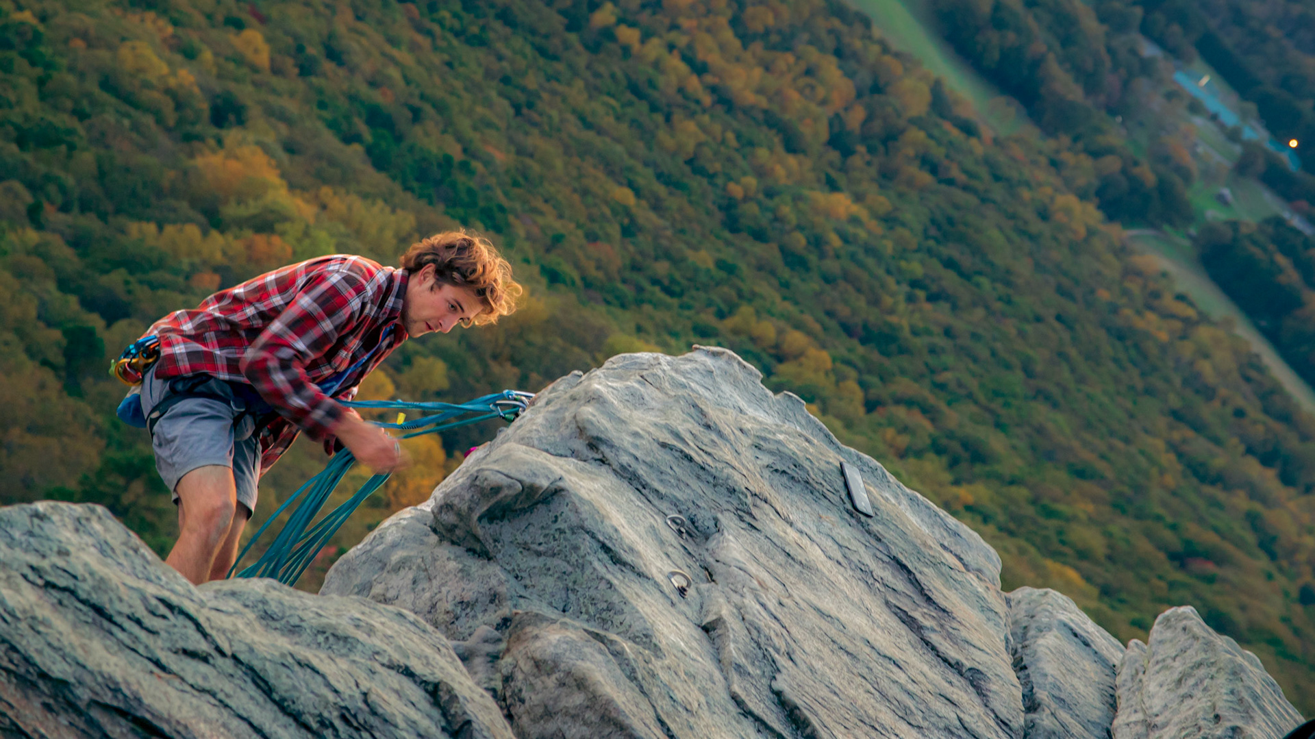 A person in a checkered handing from the side a cliff.