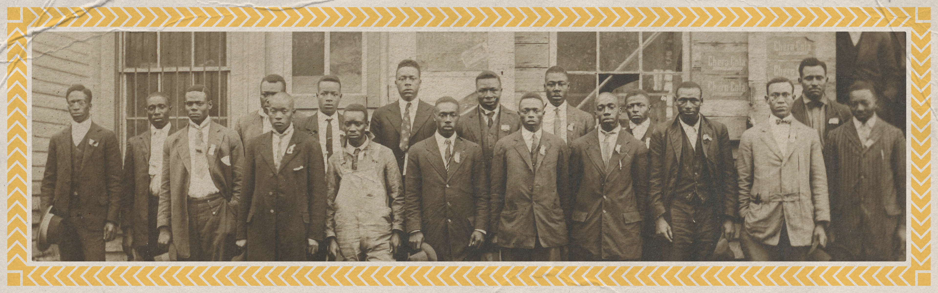 A group of men standing in front of a building with a yellow geometric border around the photo.
