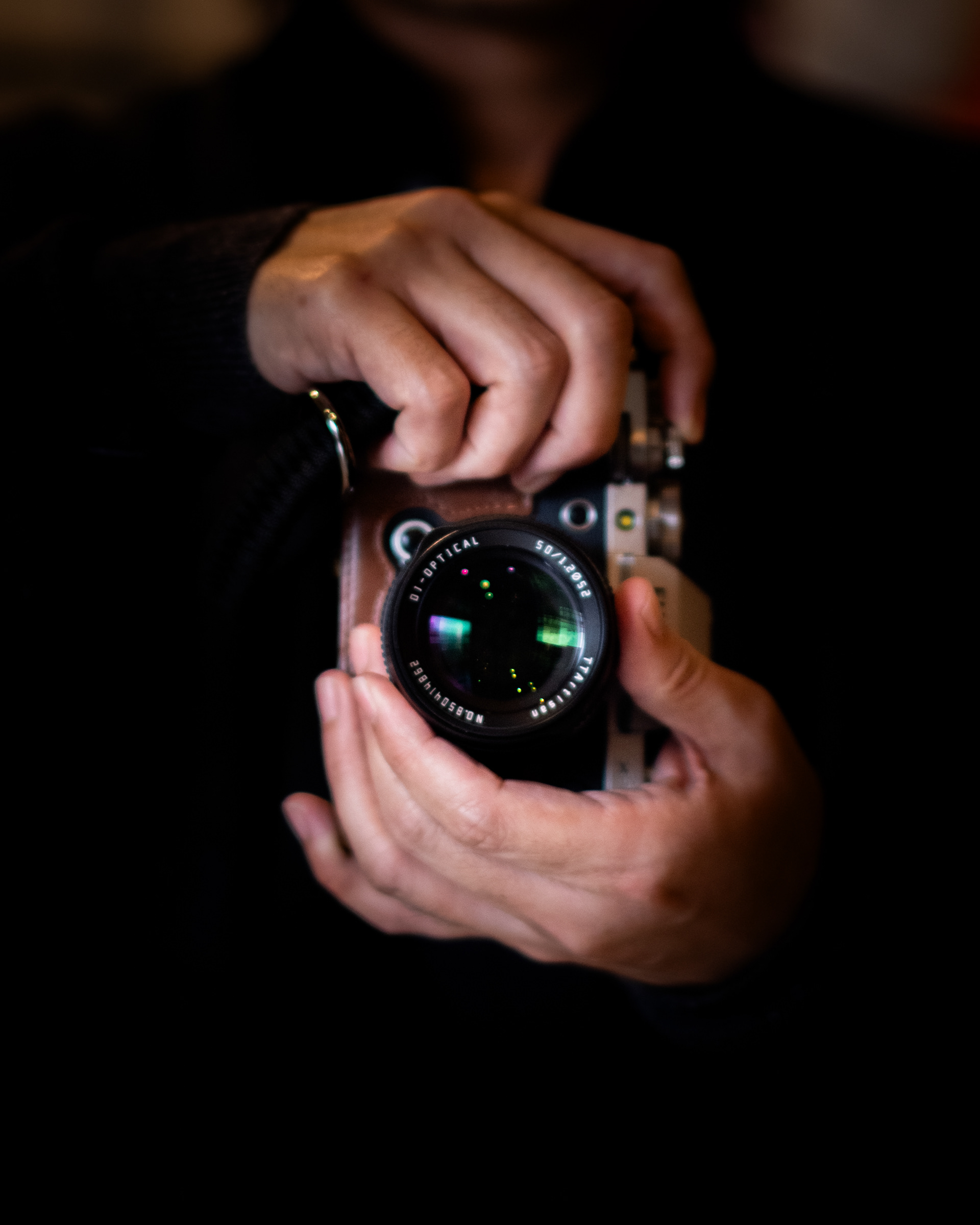 A person holding a camera close to their chest, hands gently wrapped around the lens, against a dark background.