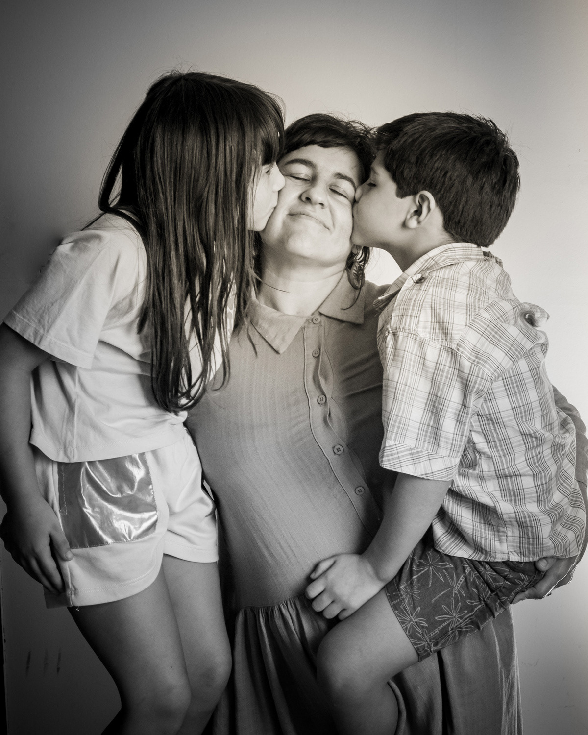 Afecto en estudio, una mamá con sus hijos, cada uno le da un beso en cada mejilla. Fotografía de Pau Aiello.