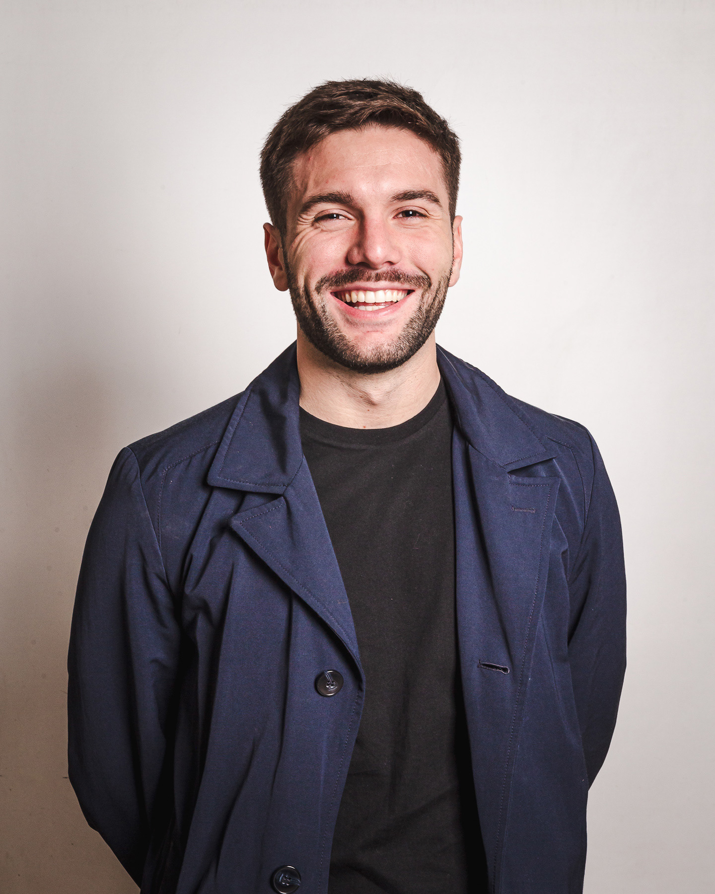 Retrato en estudio de un hombre joven de unos 30 años, sonriente y espontáneo, sobre fondo blanco grisáceo, realizado por Pau Aiello fotógrafa en Buenos Aires.