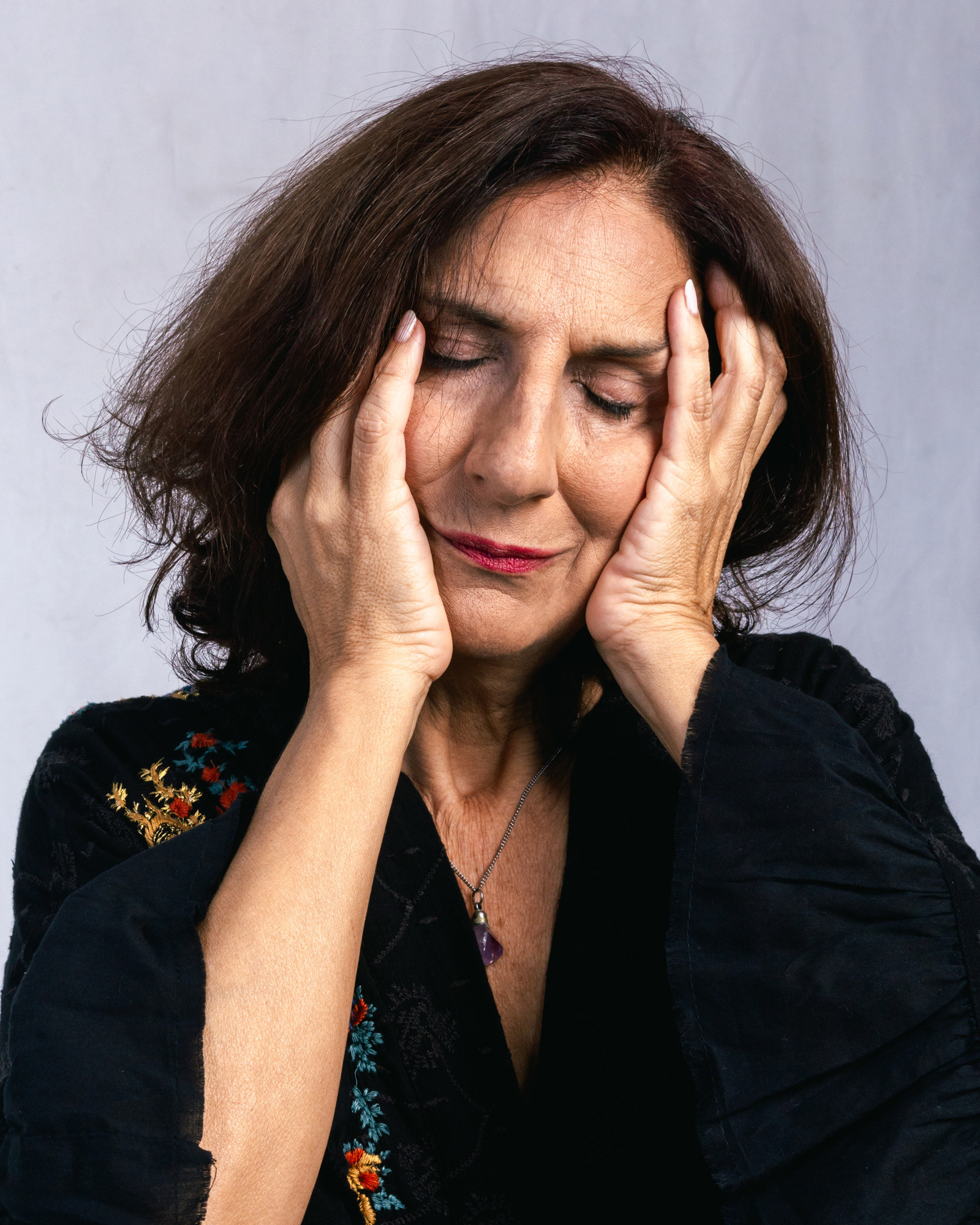 Retrato en estudio de una actriz con ojos cerrados, sosteniendo su rostro con ambas manos en un gesto de introspección profunda. Fotografía de Pau Aiello.