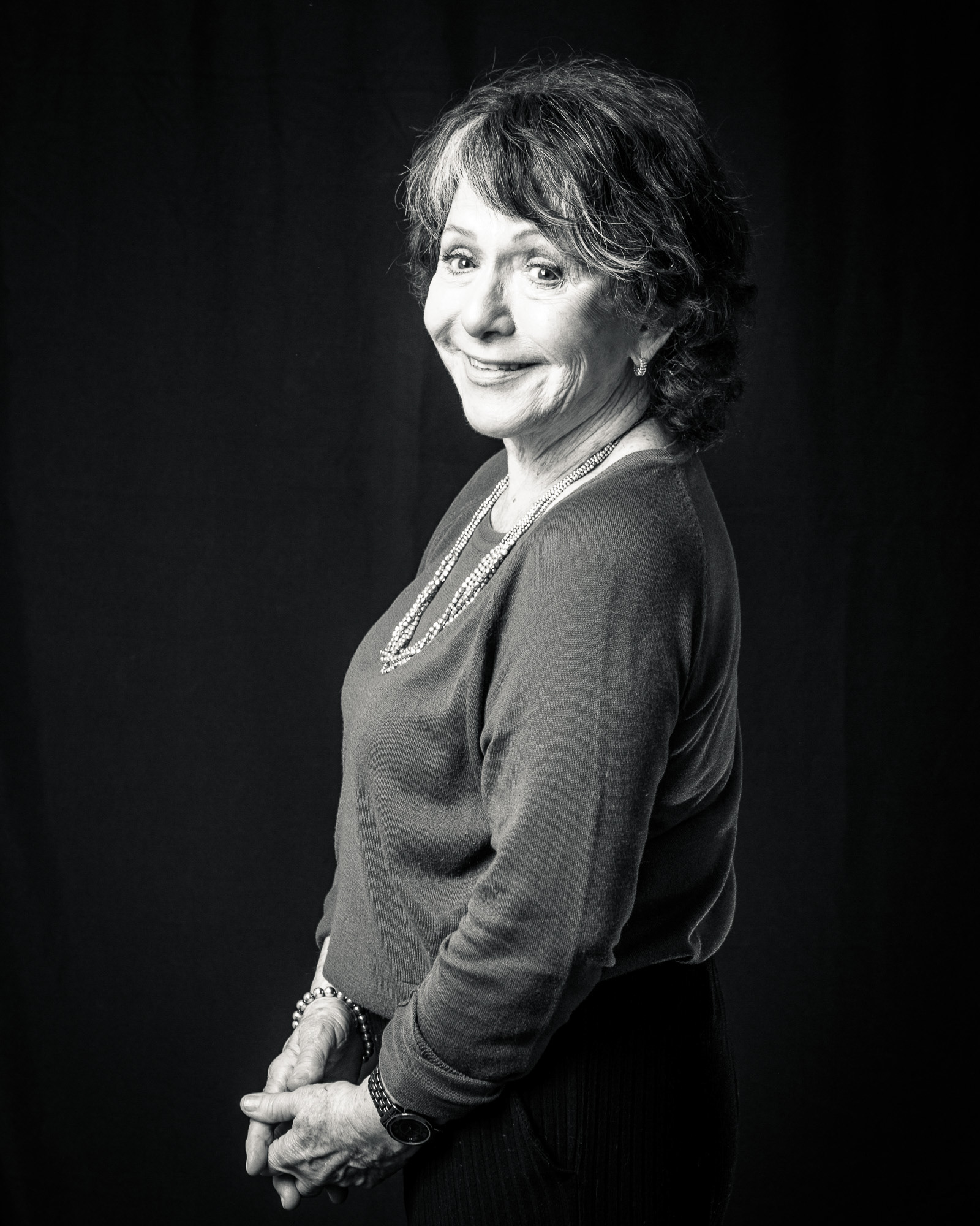 Retrato clásico en blanco y negro de una mujer mayor sonriendo a la cámara con calidez, sobre un fondo negro. Fotografía de estudio por Pau Aiello.