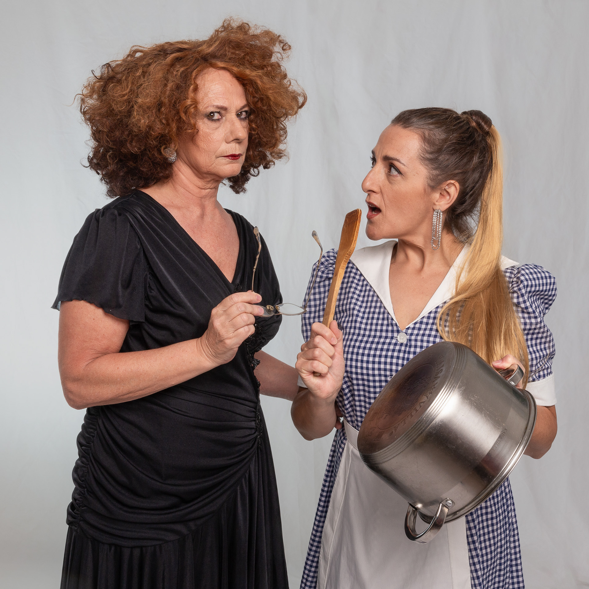 Las actrices Gimena Riestra y Carolina Alberdi interpretando a sus personajes de la obra 'minucias' en una sesión de fotos de estudio, con una expresión de conflicto cómico. Fotografía de Pau Aiello.