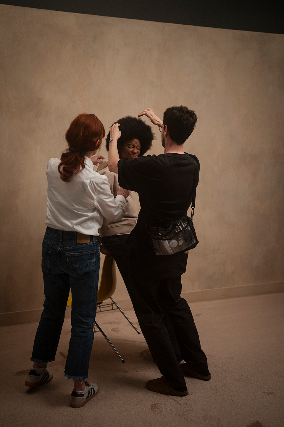 Stylisten passen Outfit und Haare des Models mit Afro nahe gelbem Stuhl in hinter den Kulissen Session der LUISA CERANO Frühling/Sommer 2026 an