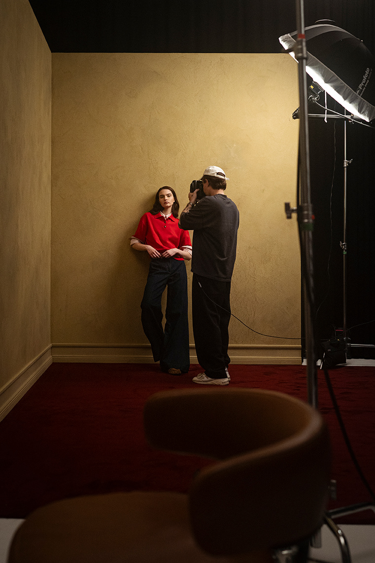 Hinter den Kulissen der LUISA CERANO Frühling/Sommer 2026: Mode-Model in rotem Polo und ausgestellten Jeans posiert, während Fotograf im Studio aufnimmt
