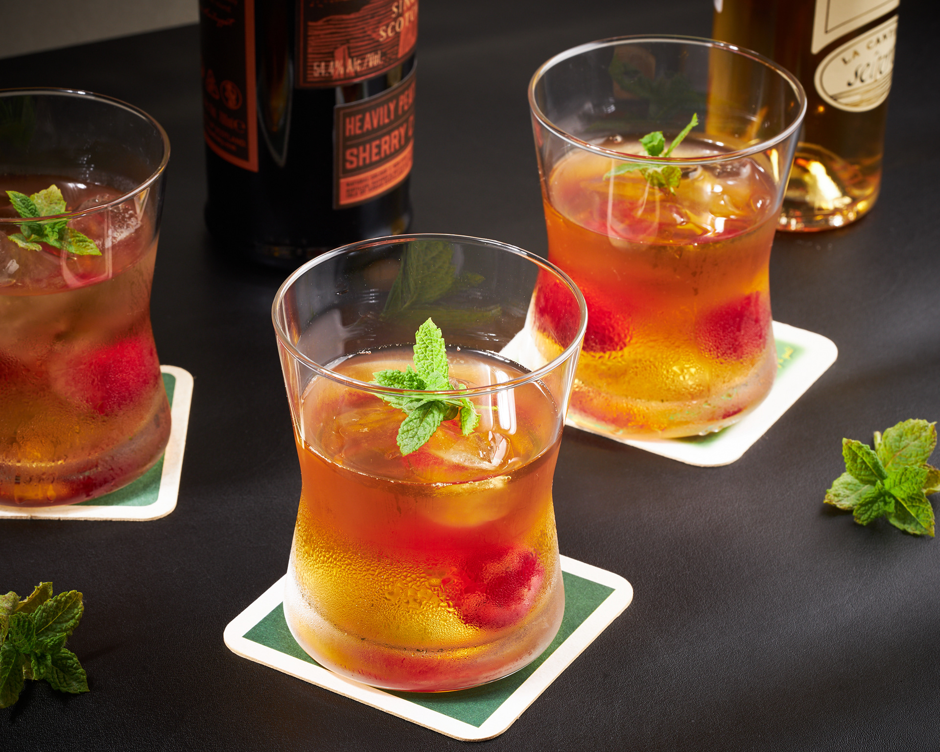 Vibrant shot of cocktail glasses with liquers in the background, on a black leather-like fabric. Image by Stefania Calderara